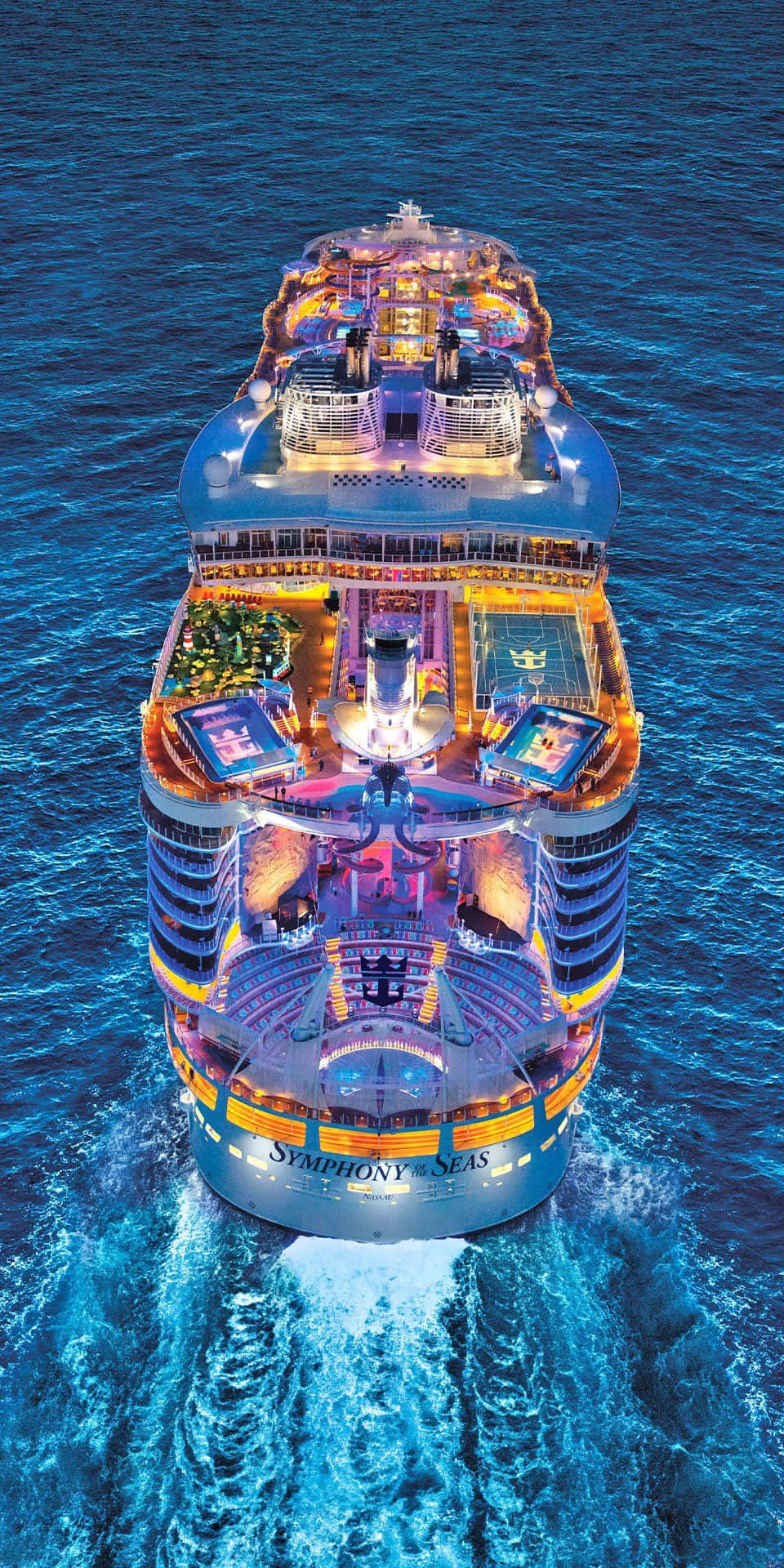 探索這艘精緻的嘉年華 Vista 航海巨艦 壁紙 — 海洋交響號郵輪在深藍色海水上閃爍著溫暖燈光的鳥瞰圖。