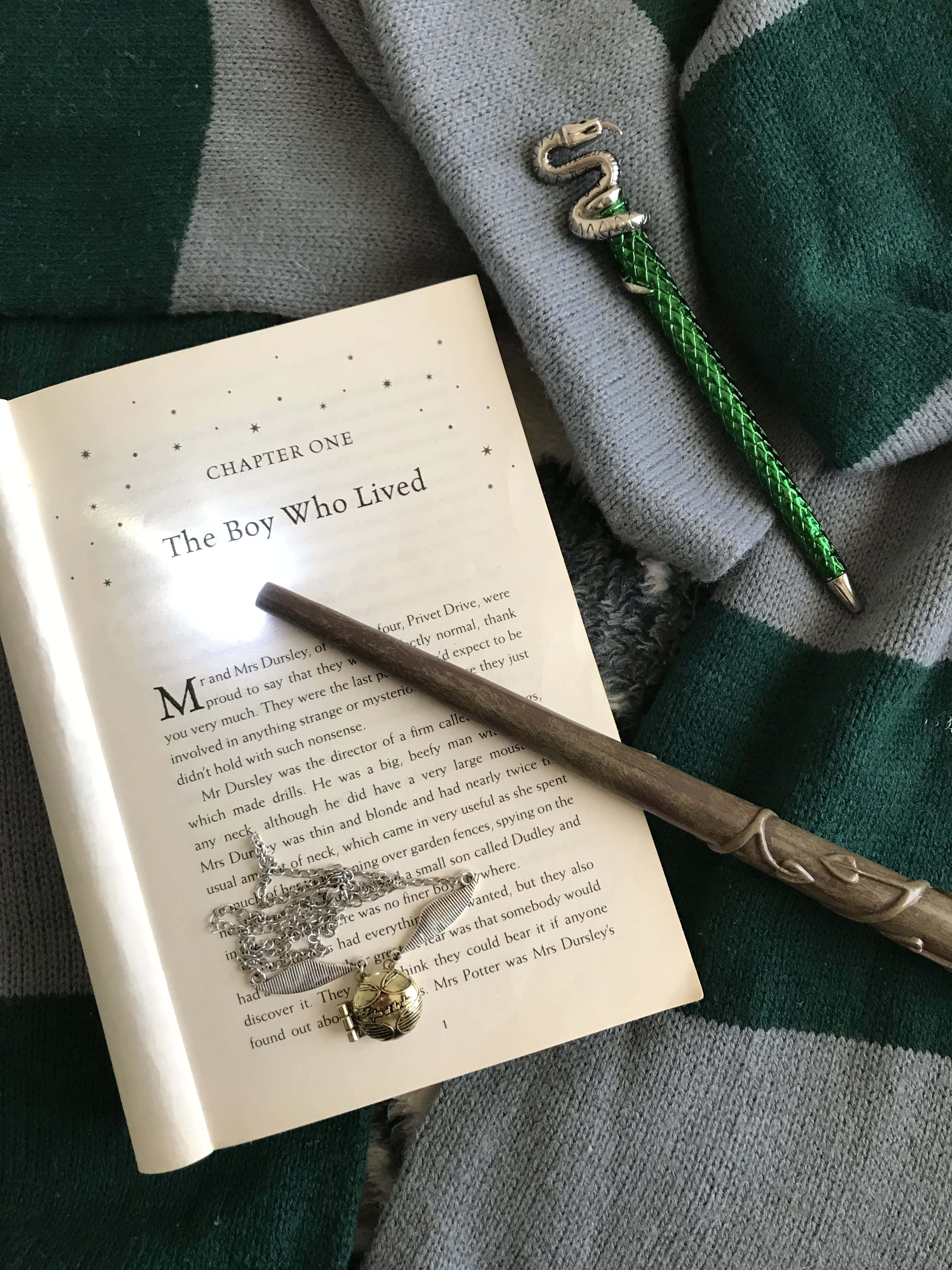探索霍格華茲的迷人領域 壁紙 — 一本打開的哈利波特書放在綠色格子毯上，旁邊有一根魔杖和一個銀色蛇形別針。