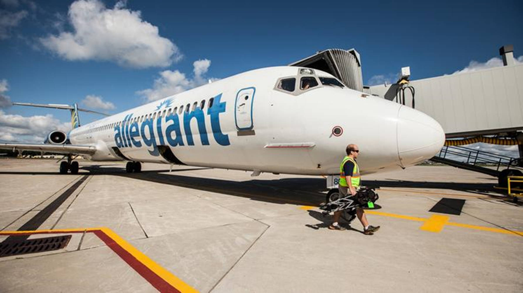 地勤人員在機場閘口附近推著行李車，靠近Allegiant飛機。