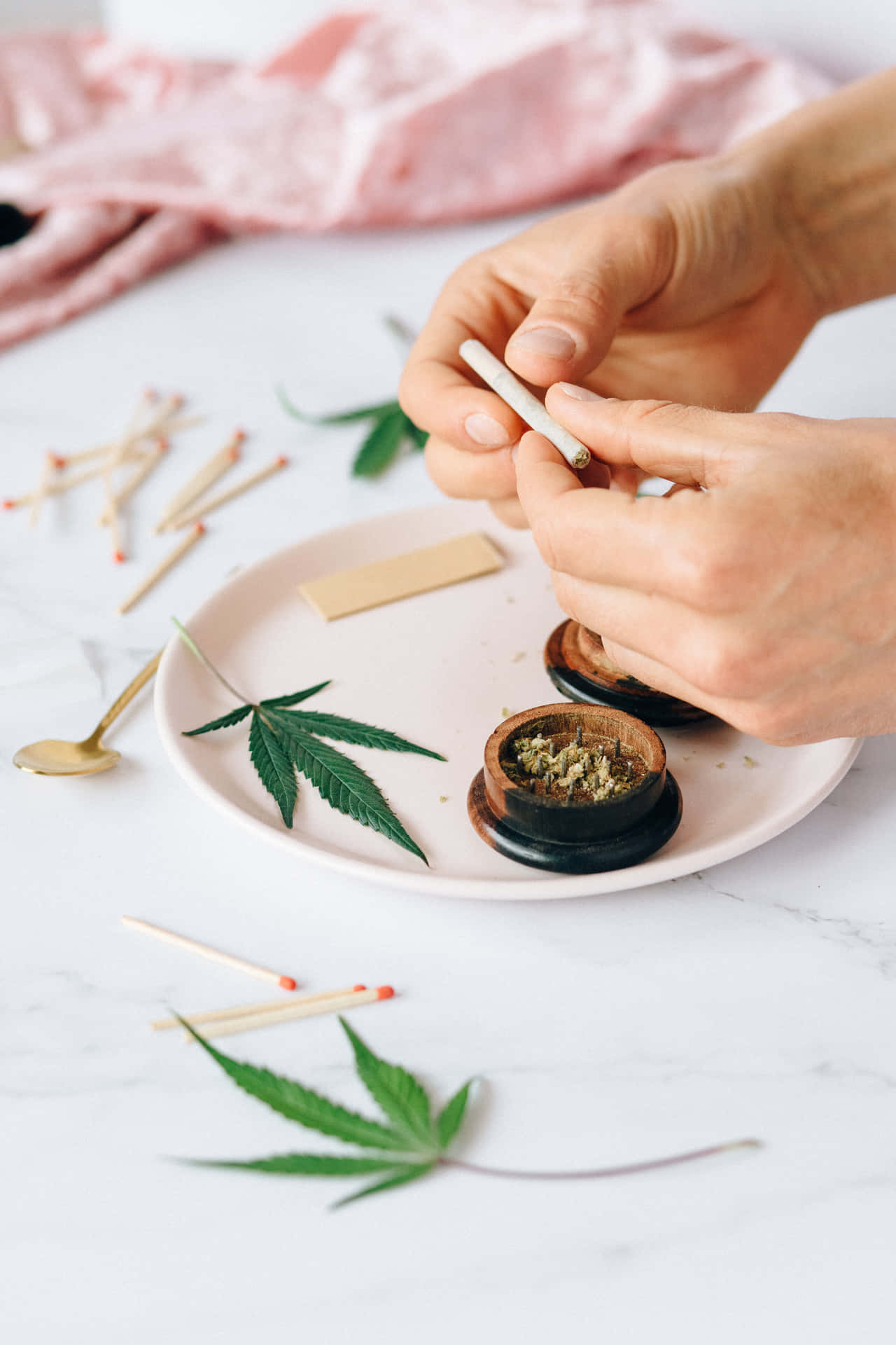 雙手在大理石表面上捲大麻煙，伴有綠葉和火柴。