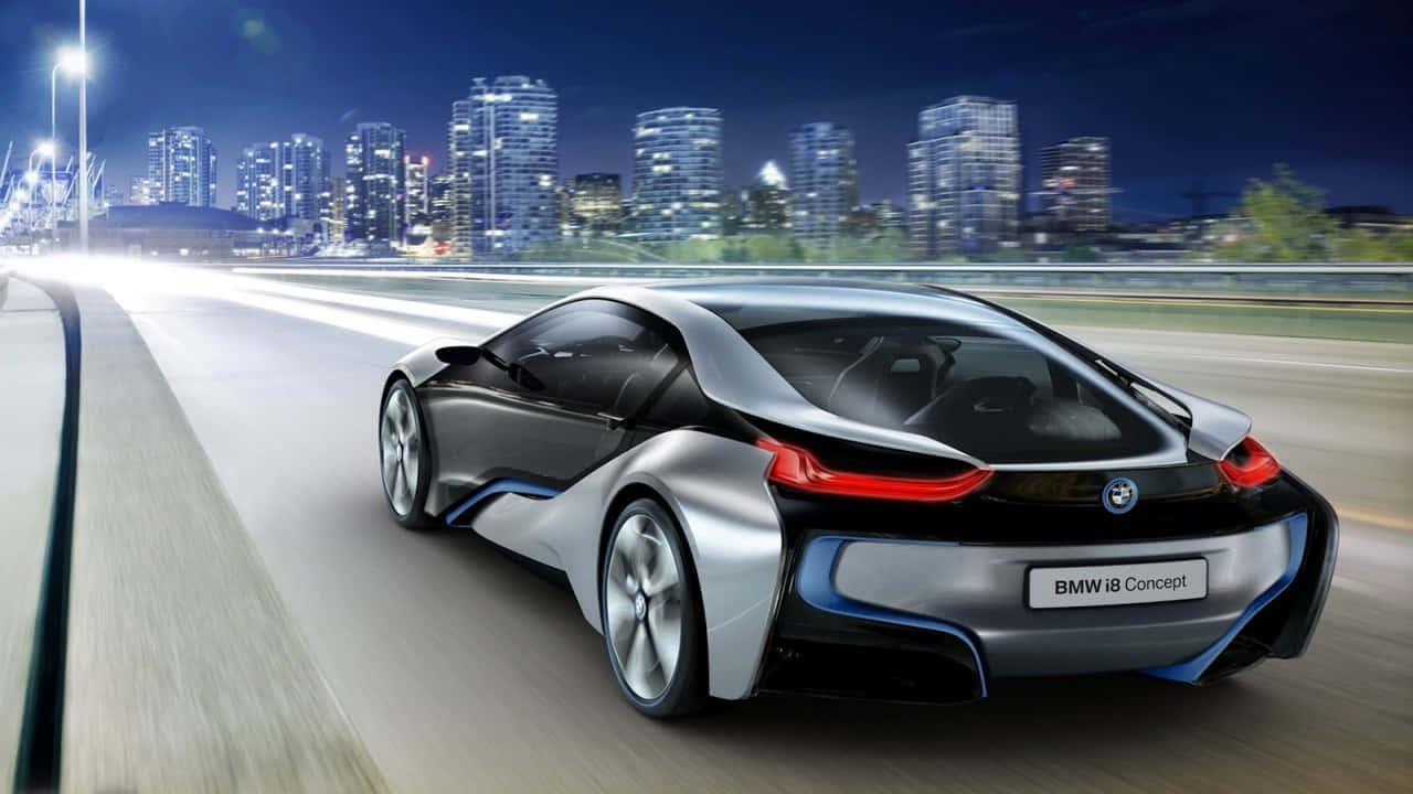 提升日常品味：720p高解析度BMW 壁紙 — 一輛時尚的銀色BMW i8概念車在夜間沿著城市高速公路行駛，背景是閃閃發光的摩天大樓。