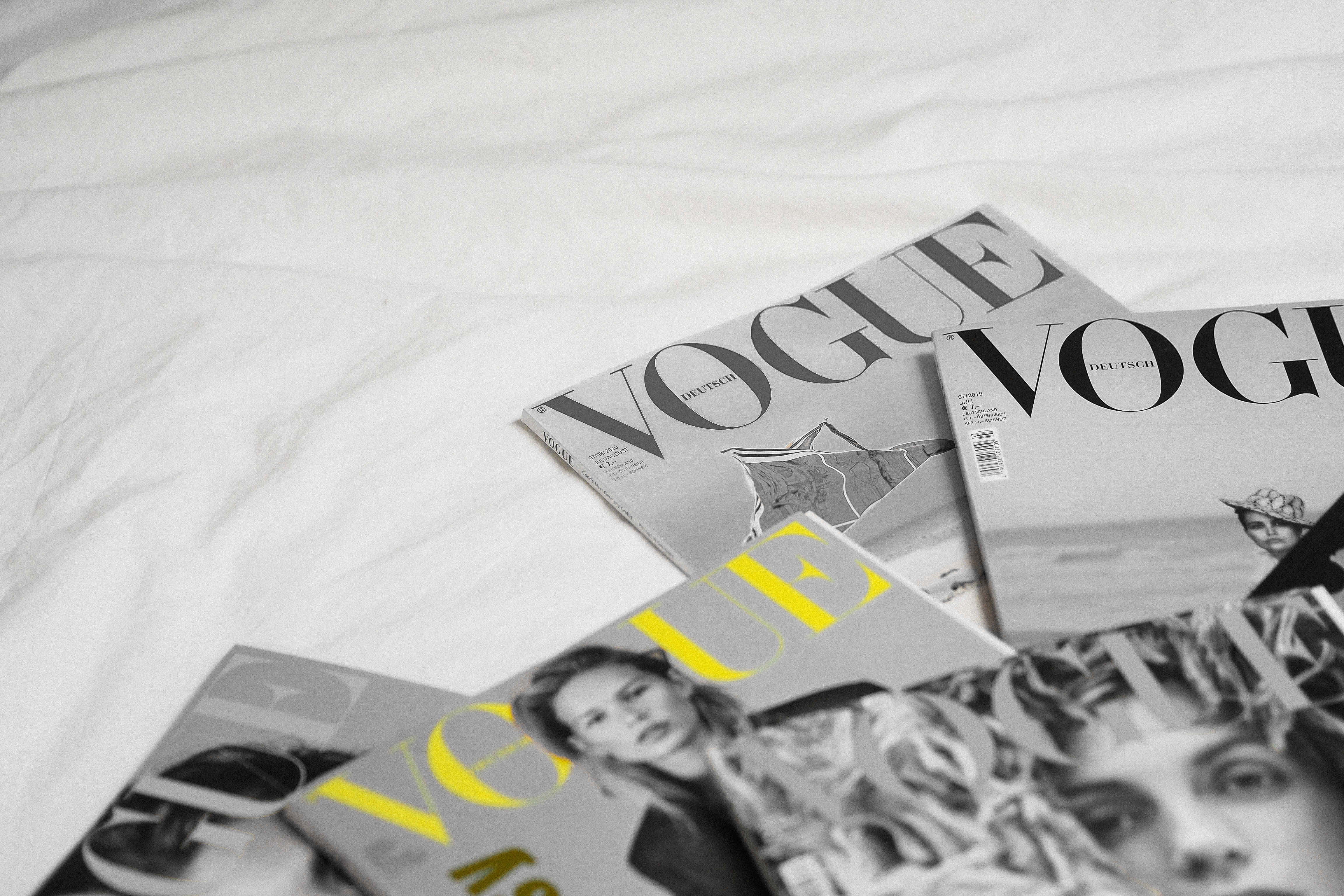 提升知識，保持資訊更新 壁紙 — 幾本Vogue雜誌，帶有粗體字體和時尚圖像，隨意地放在皺巴巴的白色床單上。