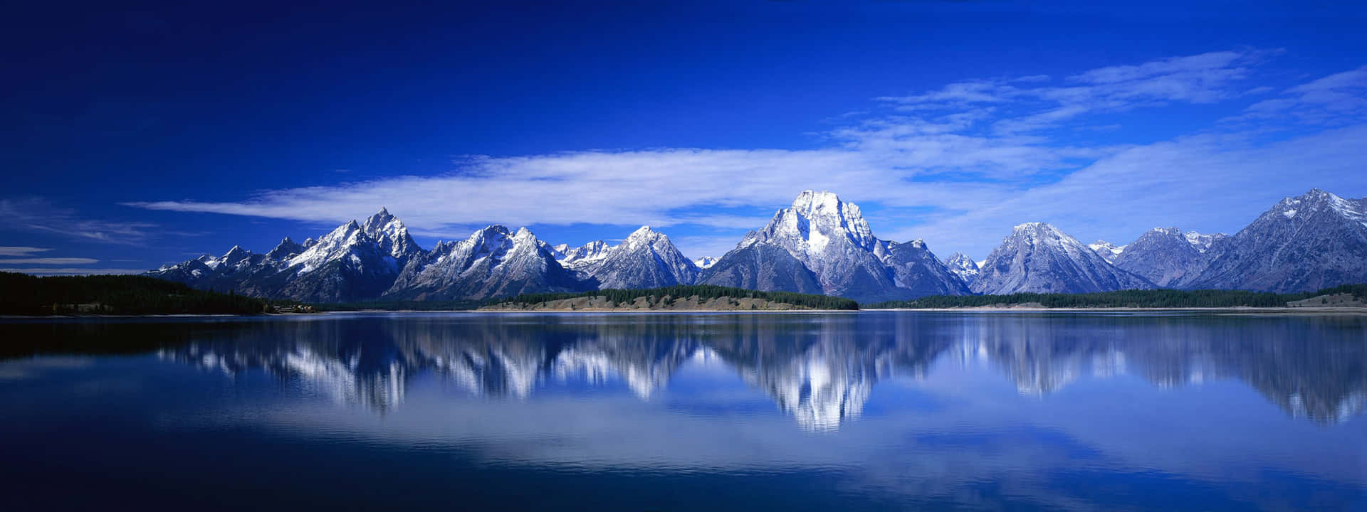 白雪皚皚的山脈在晴朗的天空下倒映在寧靜的藍色湖泊中。