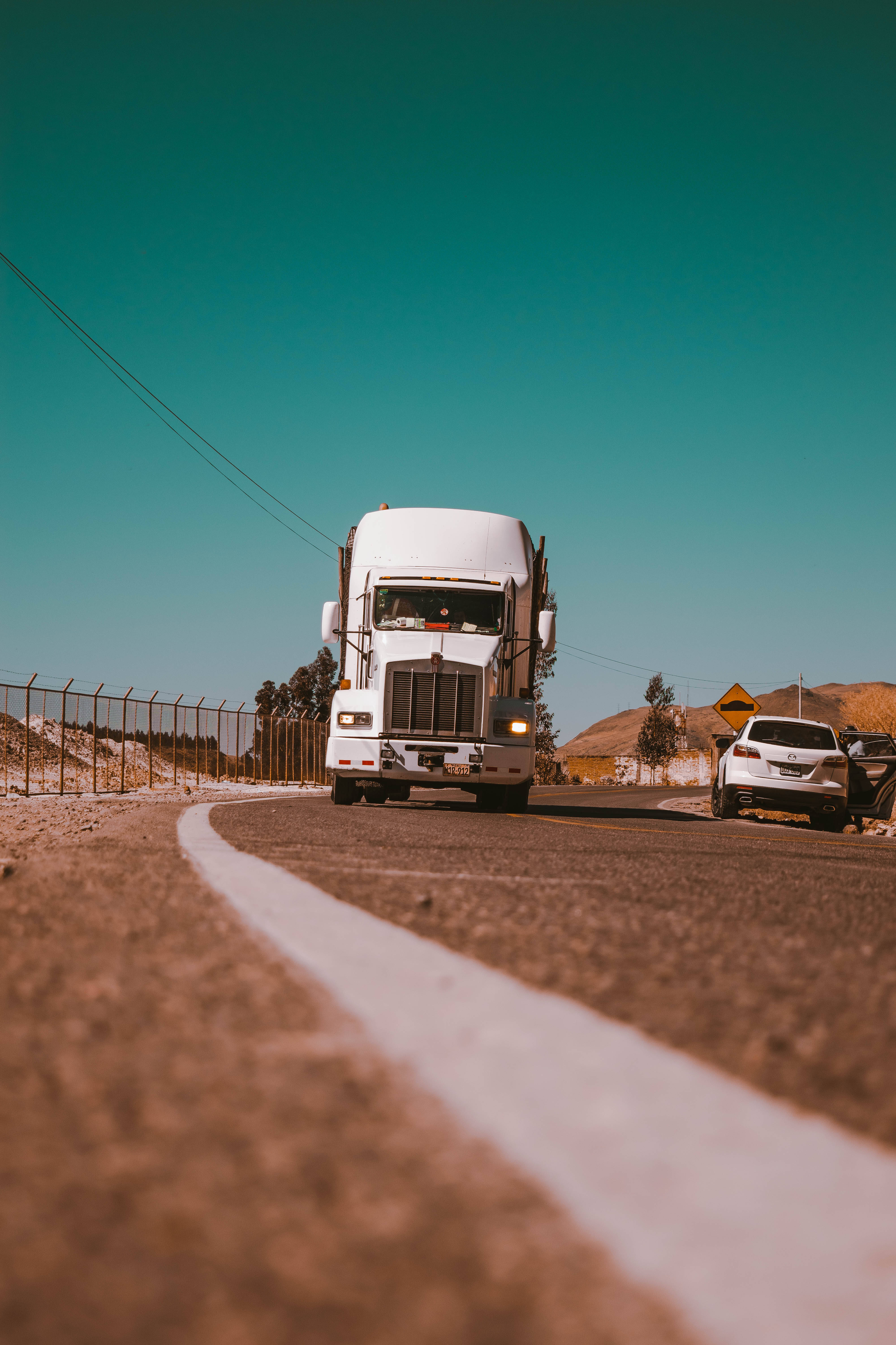 提卡潘帕區道路上的白色卡車 壁紙 — 一輛白色半掛卡車在鮮豔的青綠色天空下主宰沙漠高速公路，附近停著一輛銀色SUV。