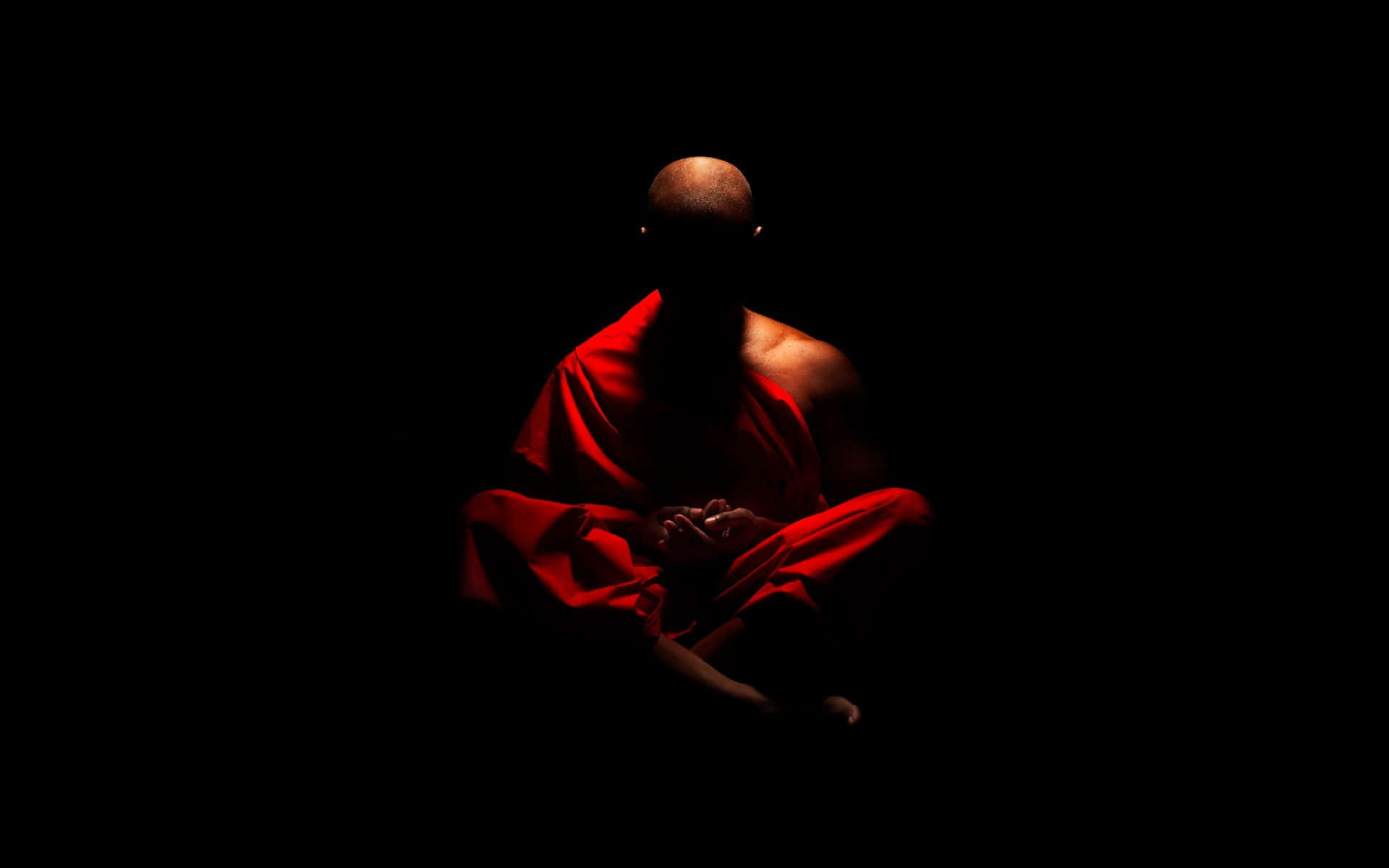 提醒我們保持平靜與寧靜的靈性風景 壁紙 — 一位身穿紅色長袍的僧侶在黑色背景前打坐，被戲劇性的紅光照亮。