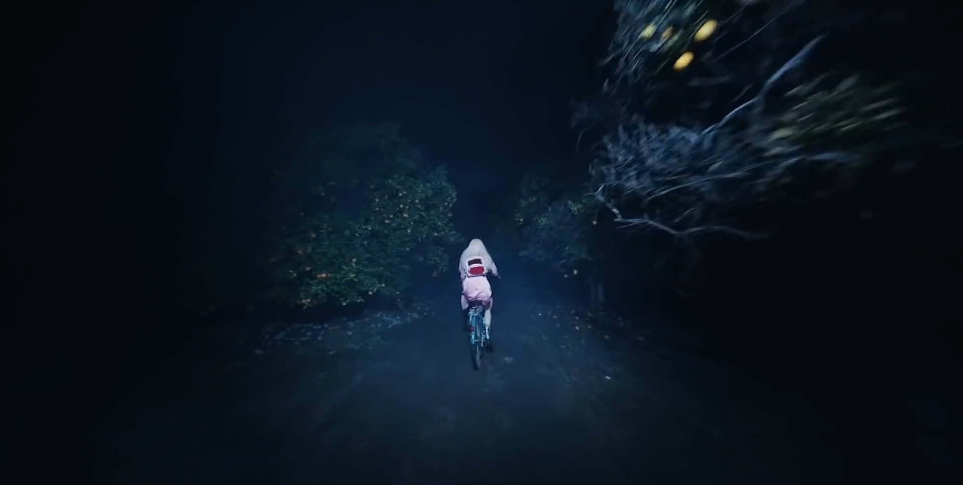 小孩騎自行車穿過黑暗森林，發光球體漂浮在附近。
