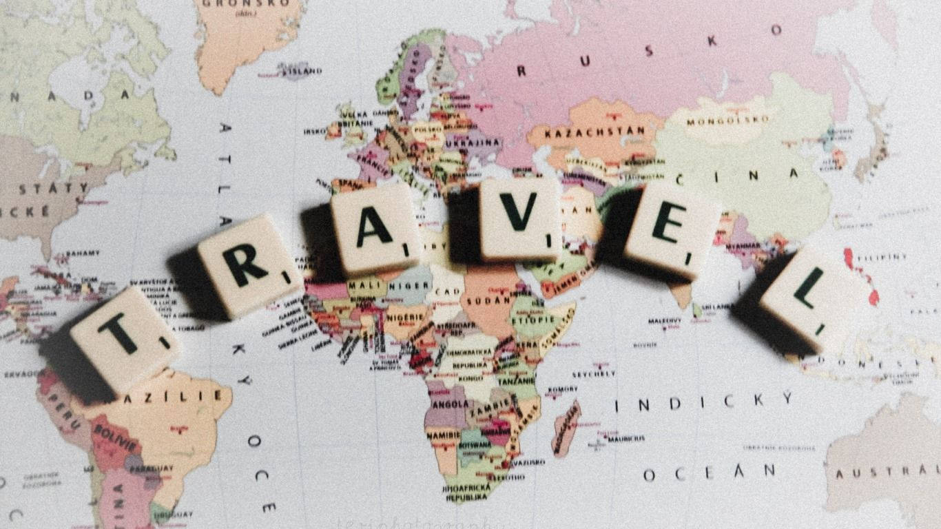 木製字母拼出「travel」喺色彩繽紛嘅世界地圖上。