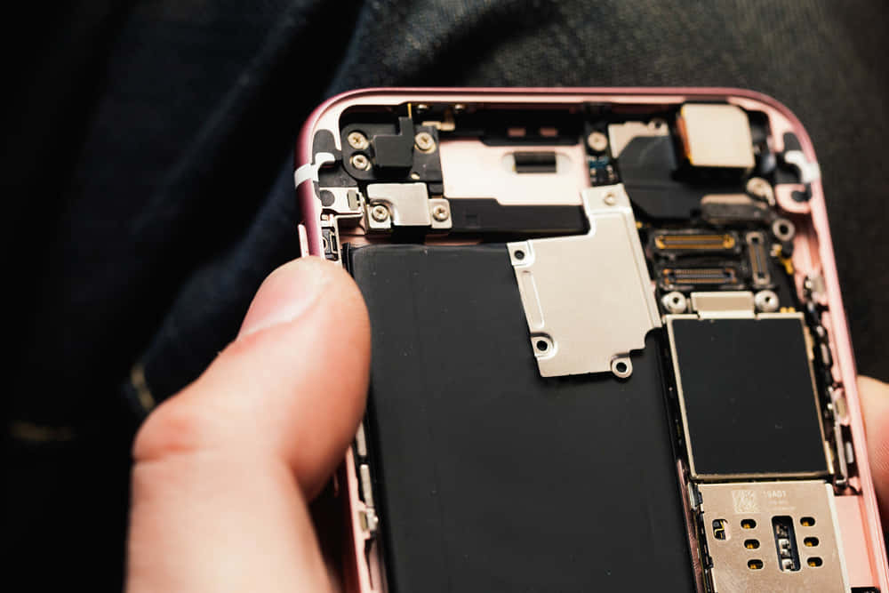 手拿著打開的粉紅色iPhone，顯示內部組件和電池。