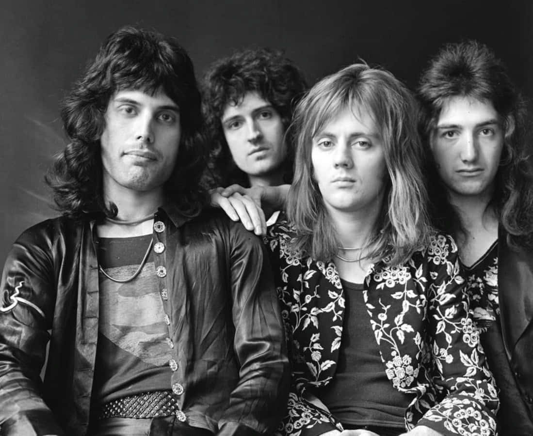 搖滾傳奇Freddie Mercury與Brian May 壁紙 — 四位長髮男士穿著70年代時裝，在黑白工作室肖像中嚴肅地擺姿勢。