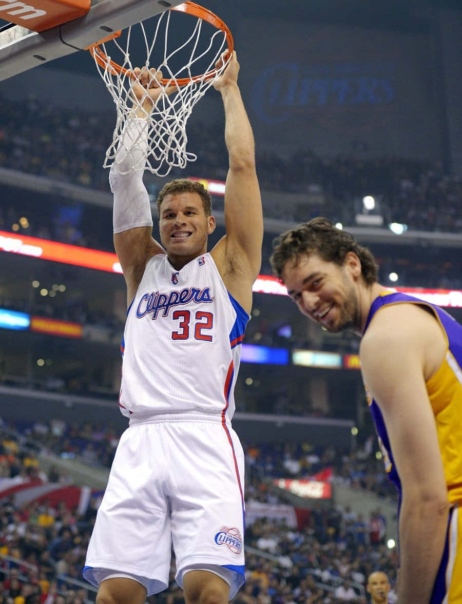 搞笑NBA球員滑稽照 壁紙 — 一位身穿快艇隊球衣的籃球運動員掛在籃框上，露出勝利的笑容，而對手在擠滿人的場館內微笑。