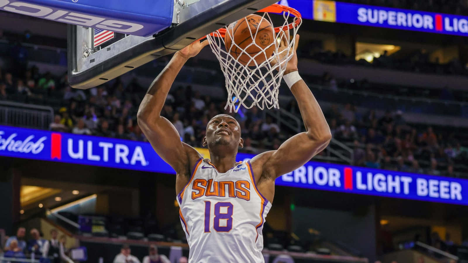 搞笑NBA籃筐懸掛圖片 壁紙 — 一名身穿白色太陽隊球衣的籃球運動員在明亮的場館燈光下，專注地灌籃。
