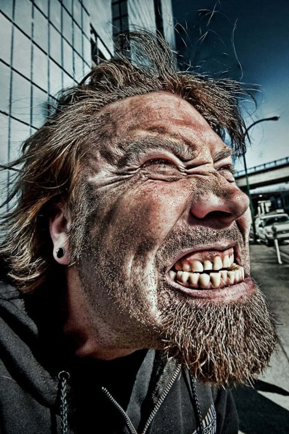 搞笑呆男搞笑表情圖 壁紙 — 一個頭髮蓬亂、鬍鬚濃密的男人在 gritty 的城市背景下激烈尖叫的特寫照片。