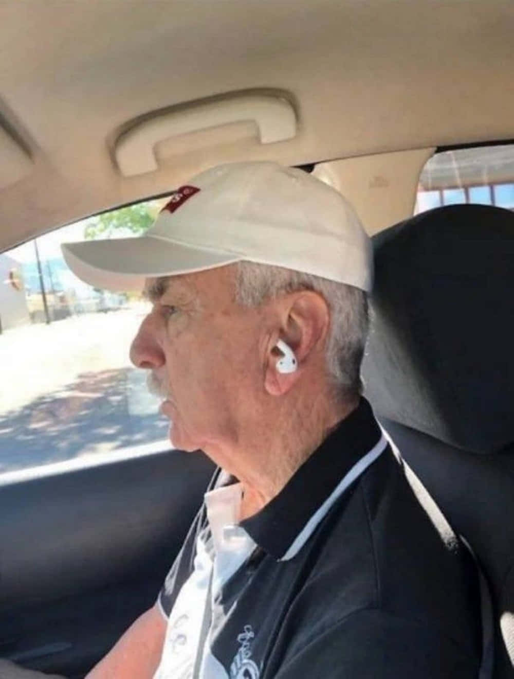 搞笑呆萌戴反耳機老翁圖 壁紙 — 一位戴著白色帽子和耳塞的年長男性坐在汽車駕駛座上向前看。