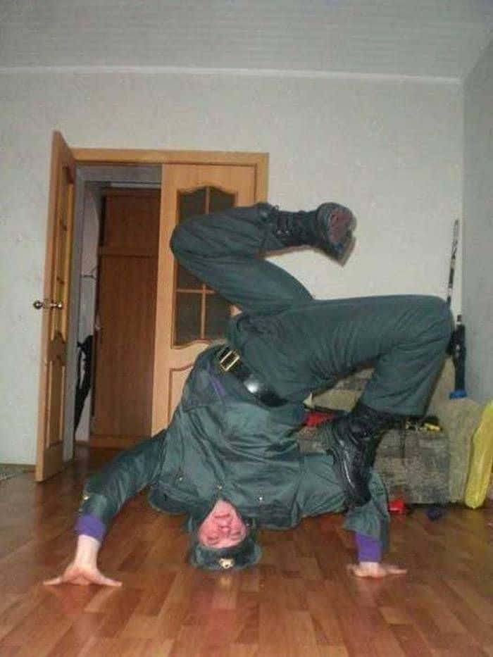 身穿綠色制服的人士在室內木地板上做倒立。