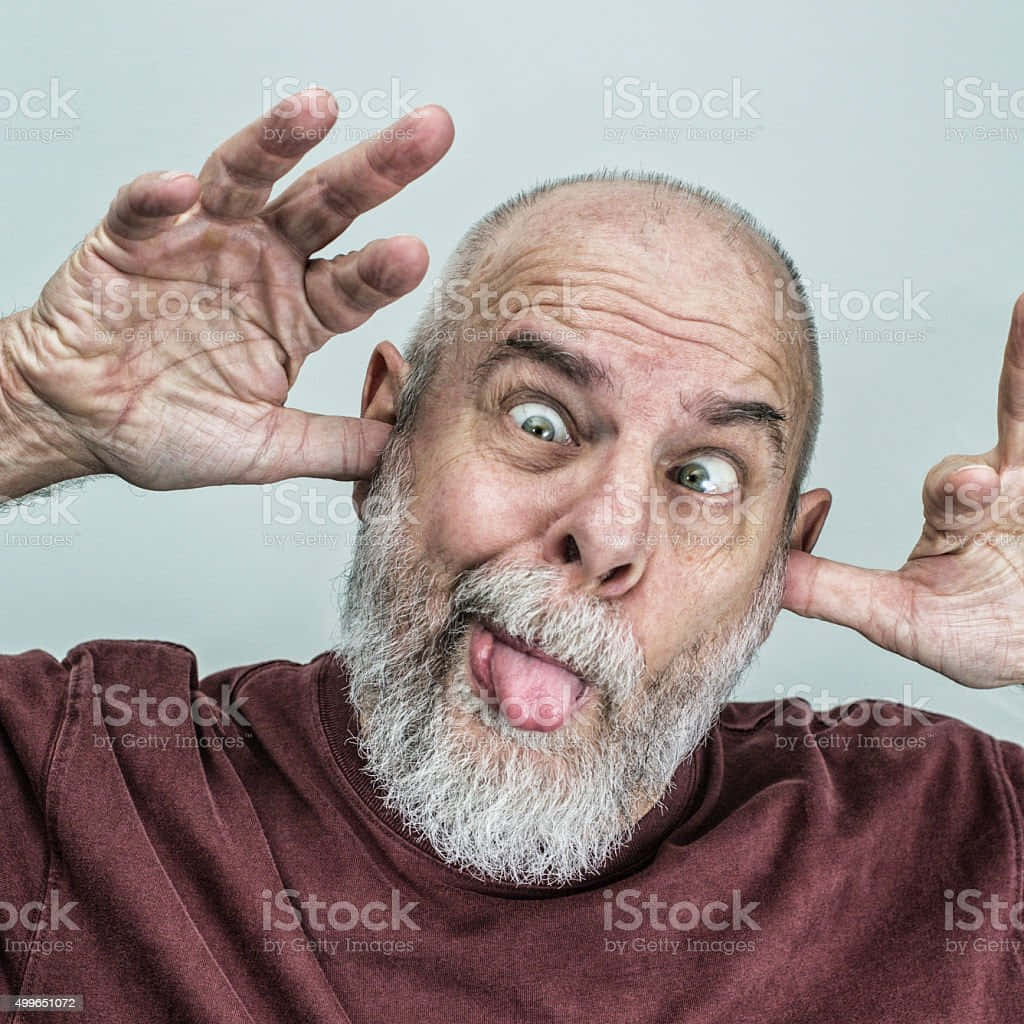 搞笑老人手指戳耳朵圖 壁紙 — 一個禿頭灰鬍鬚的男人做出一個愚蠢的表情，伸出舌頭並用雙手捂住耳朵。