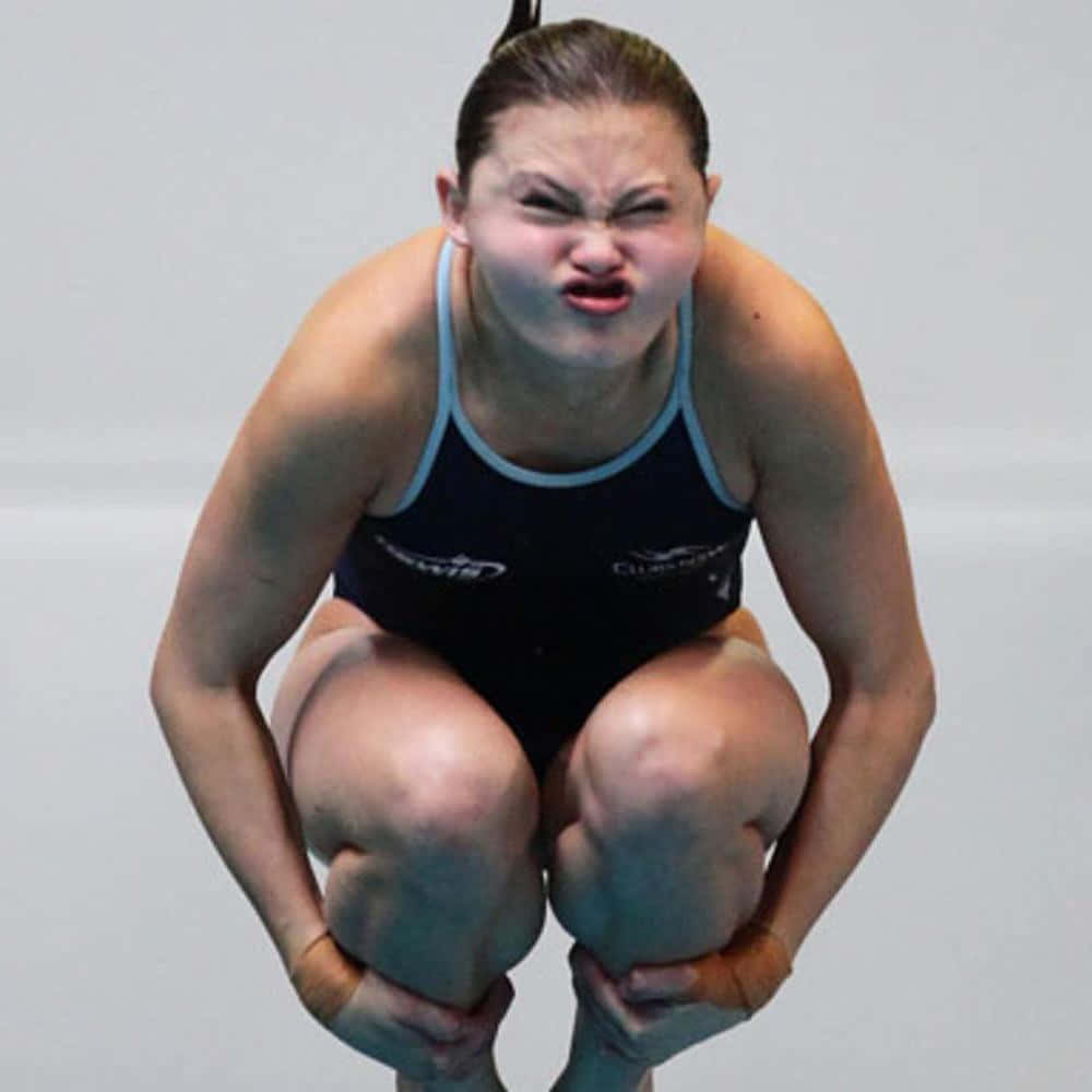 搞笑運動跳水選手的搞怪表情 壁紙 — 一名女潛水員在跳板上蹲下，專注而表情兇猛，準備跳躍。