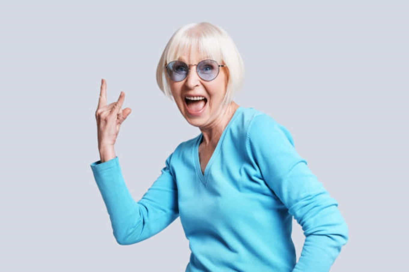穿著藍色毛衣的興奮老年女性戴著眼鏡做出搖滾手勢
