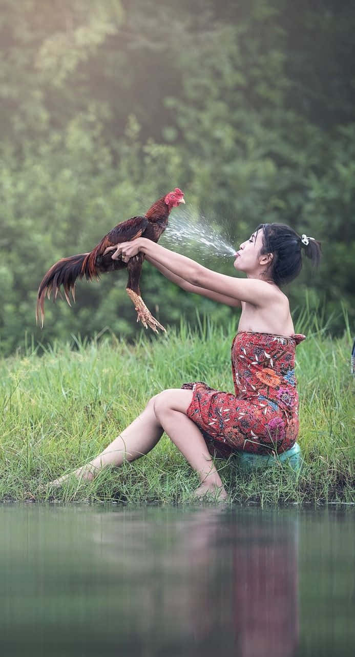 女性在水邊抱著噴水的公雞