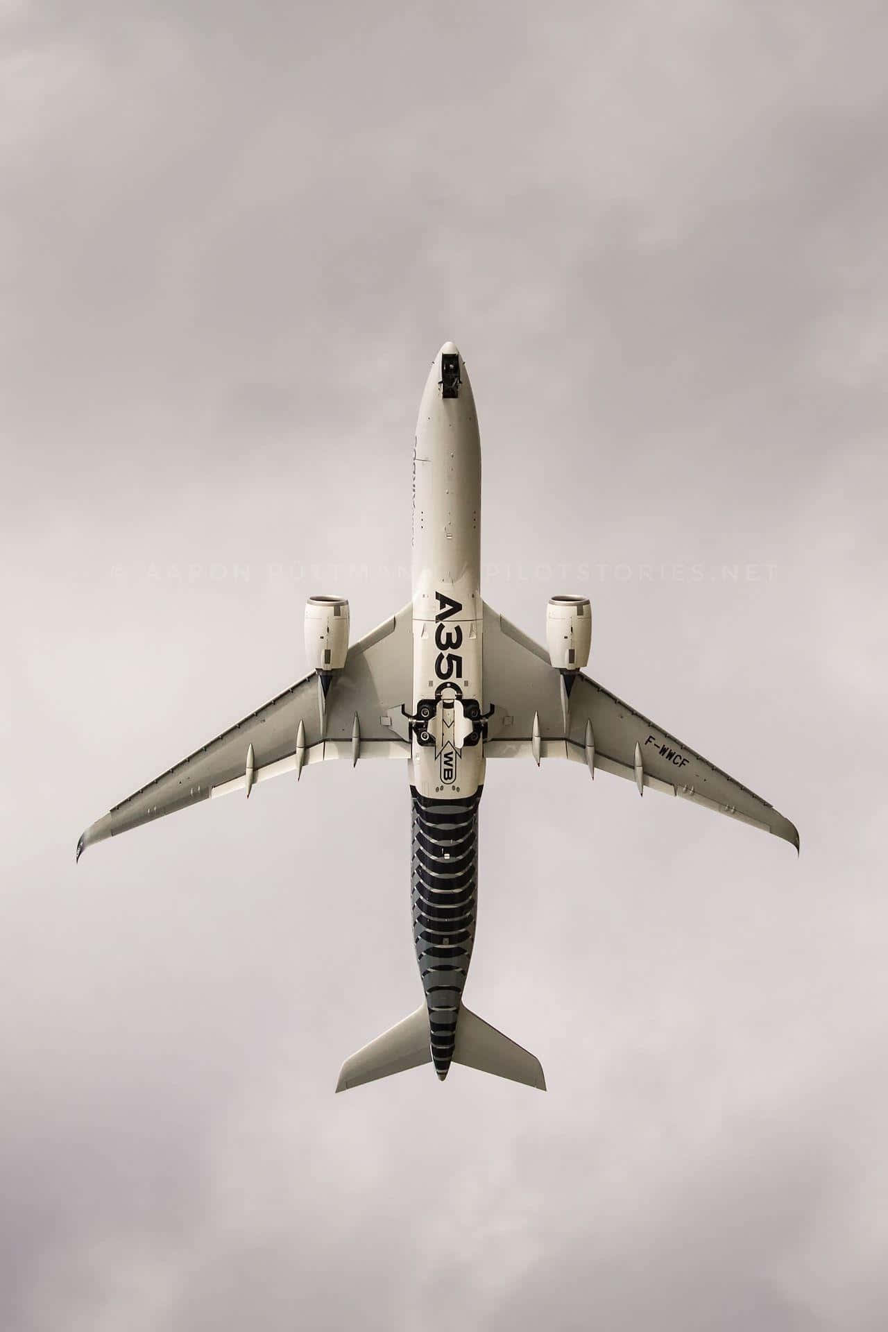 搭乘商用飛機環遊世界 壁紙 — 從上方俯瞰一架白色空中巴士A350在陰天灰色天空中飛過。