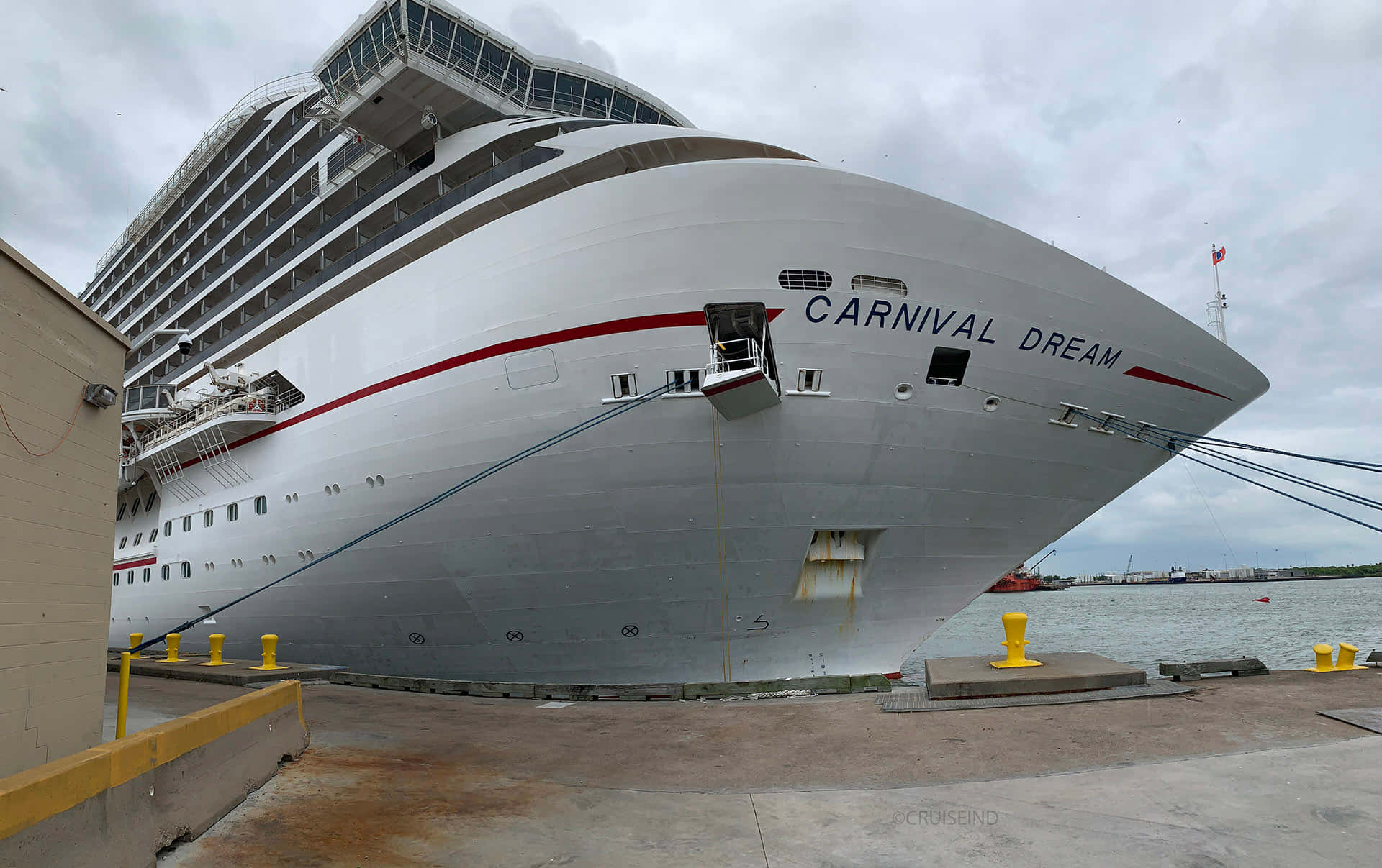 搭乘嘉年華夢幻號遊輪之旅 壁紙 — 巨大的白色郵輪 Carnival Dream 停泊在碼頭，天空多雲，船首清晰可見其名稱。