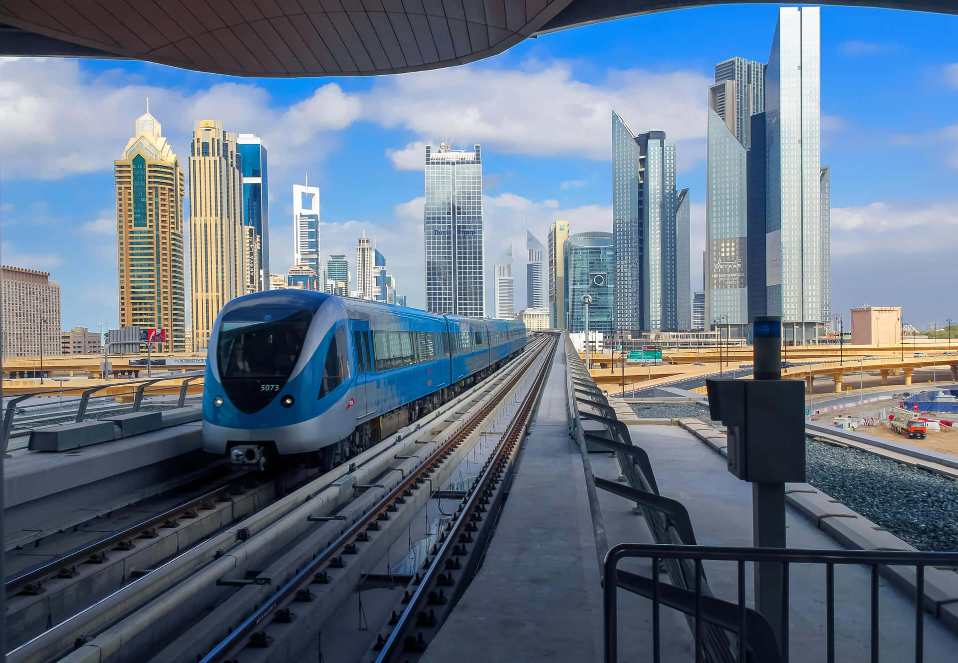 藍色地鐵列車在高架軌道上，背景有現代摩天大樓。