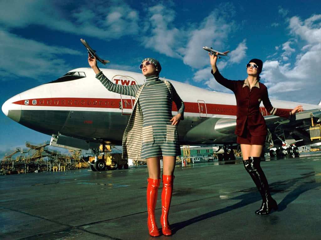 兩位復古空中服務員在停機坪上，於TWA飛機前手持玩具飛機。