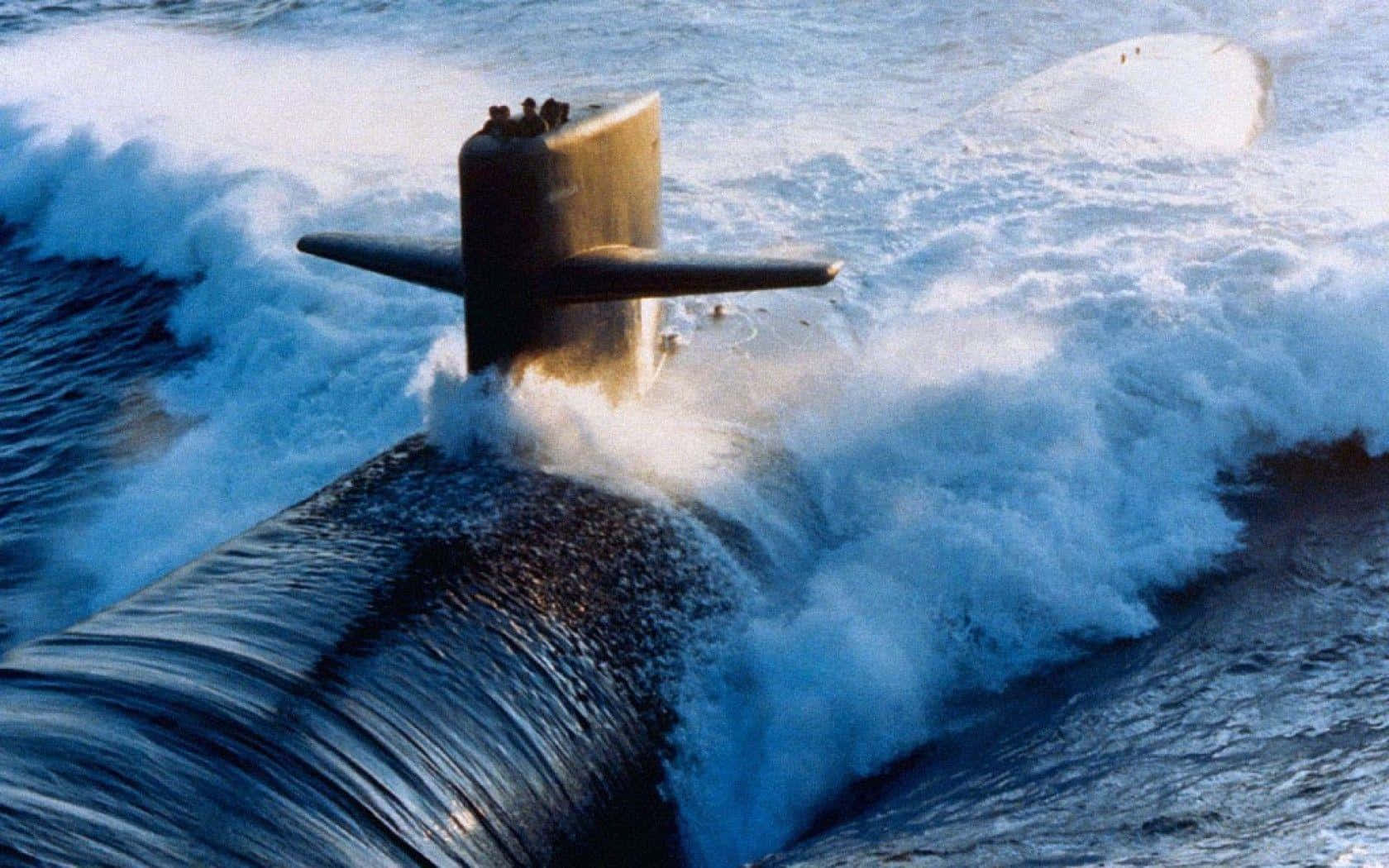 搭乘潛艇探索海底世界 壁紙 — 一艘軍用潛艇穿過洶湧的海浪浮出水面，激起戲劇性的白色泡沫。