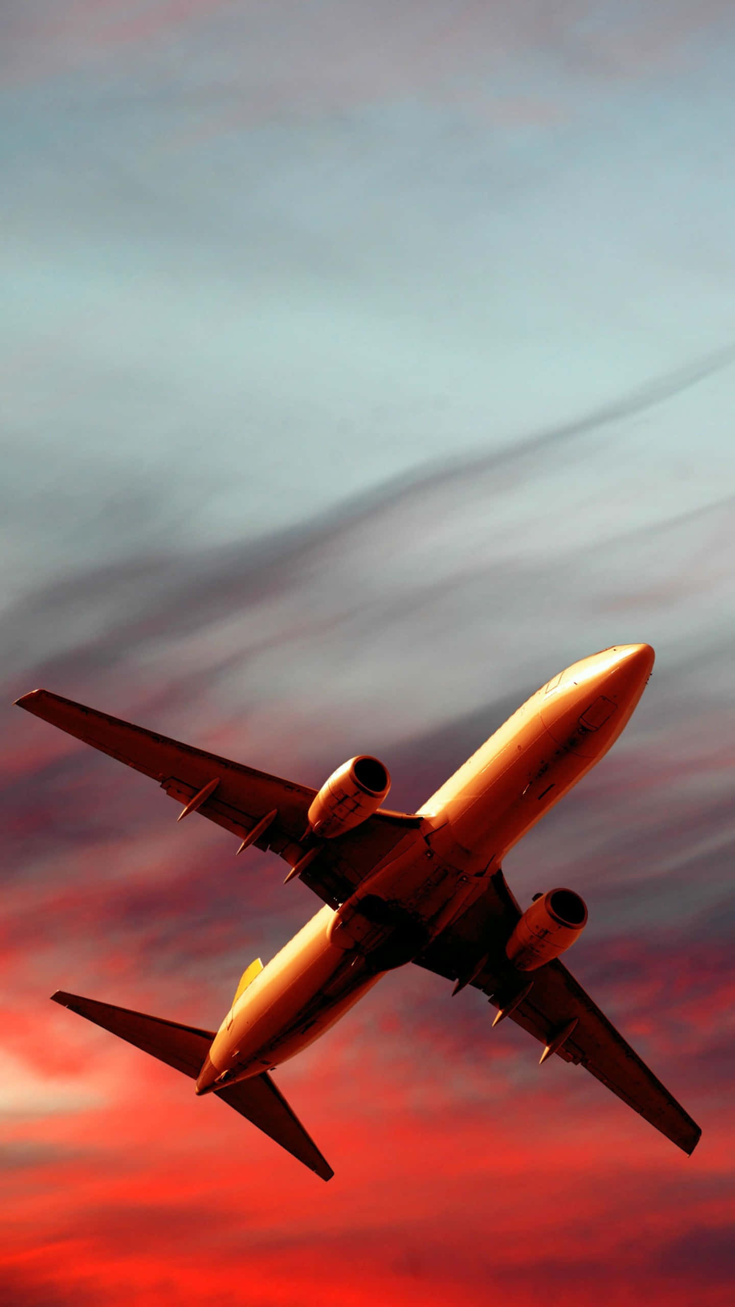 搭乘飛機翱翔天際 iPhone 壁紙 — 一架商用飛機在日落時分，於火紅與冷藍交織的戲劇性天空中翱翔。