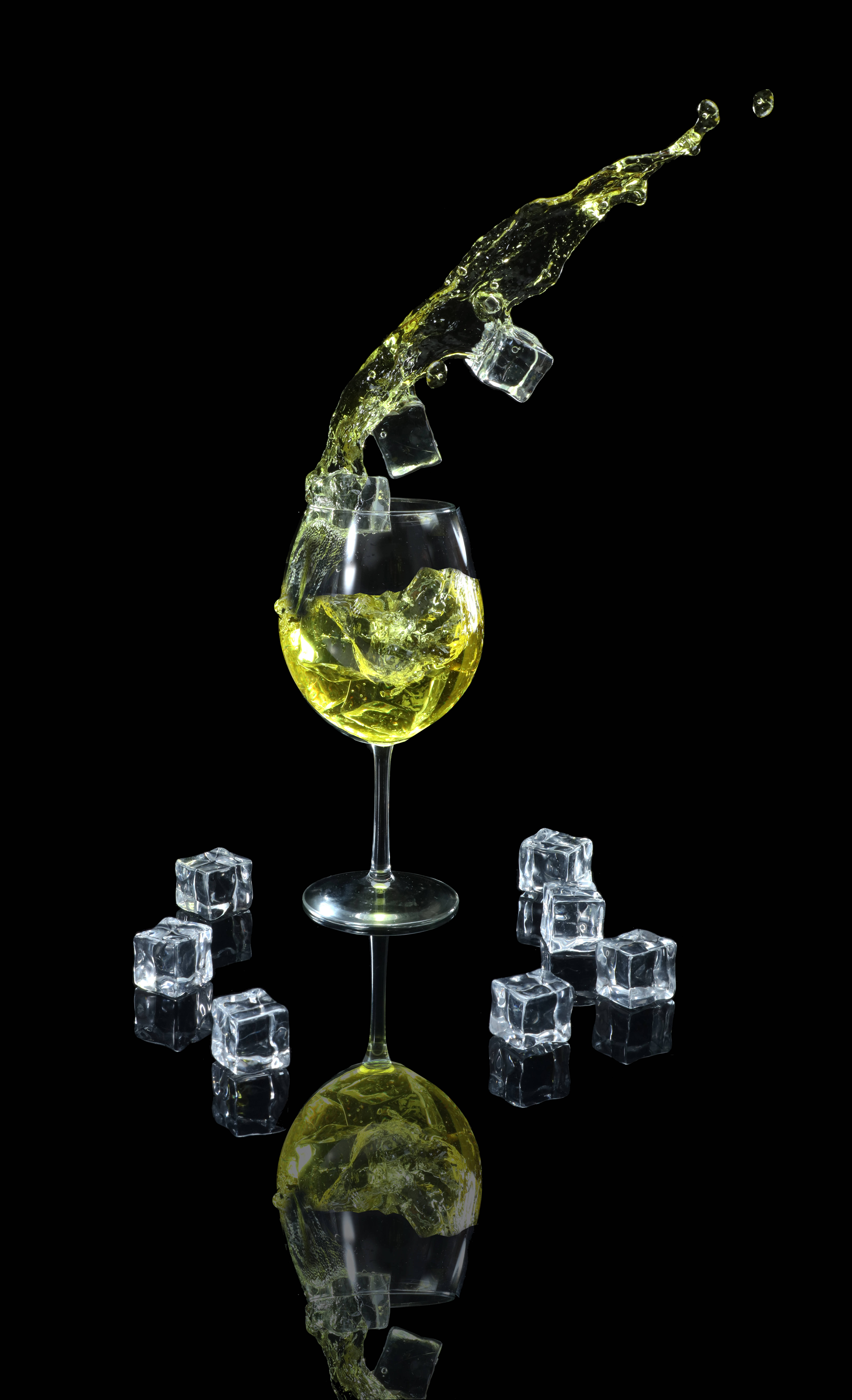 搭配冰塊的清爽雞尾酒 壁紙 — 在帶有反射表面的漆黑背景上，金色液體和冰塊從酒杯中動態噴出。