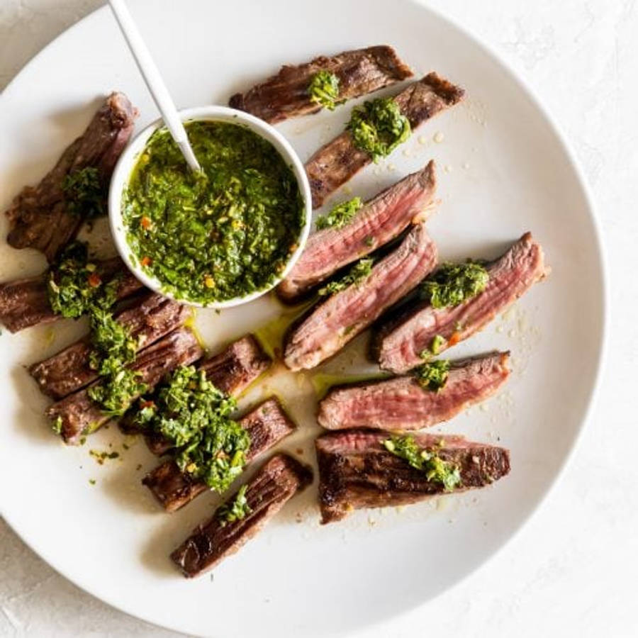 搭配奇米恰爾里醬的美味烤肉 壁紙 — 切片嘅 medium-rare 牛扒排列喺白色碟上，配上鮮綠色 chimichurri 醬。