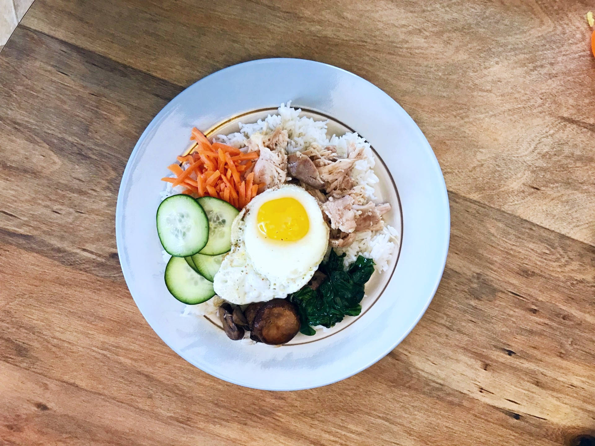 搭配新鮮蔬菜的美味韓式拌飯 壁紙 — 木桌上白色碟子盛載米飯、吞拿魚、菠菜、蘑菇、青瓜和太陽蛋的俯視圖。