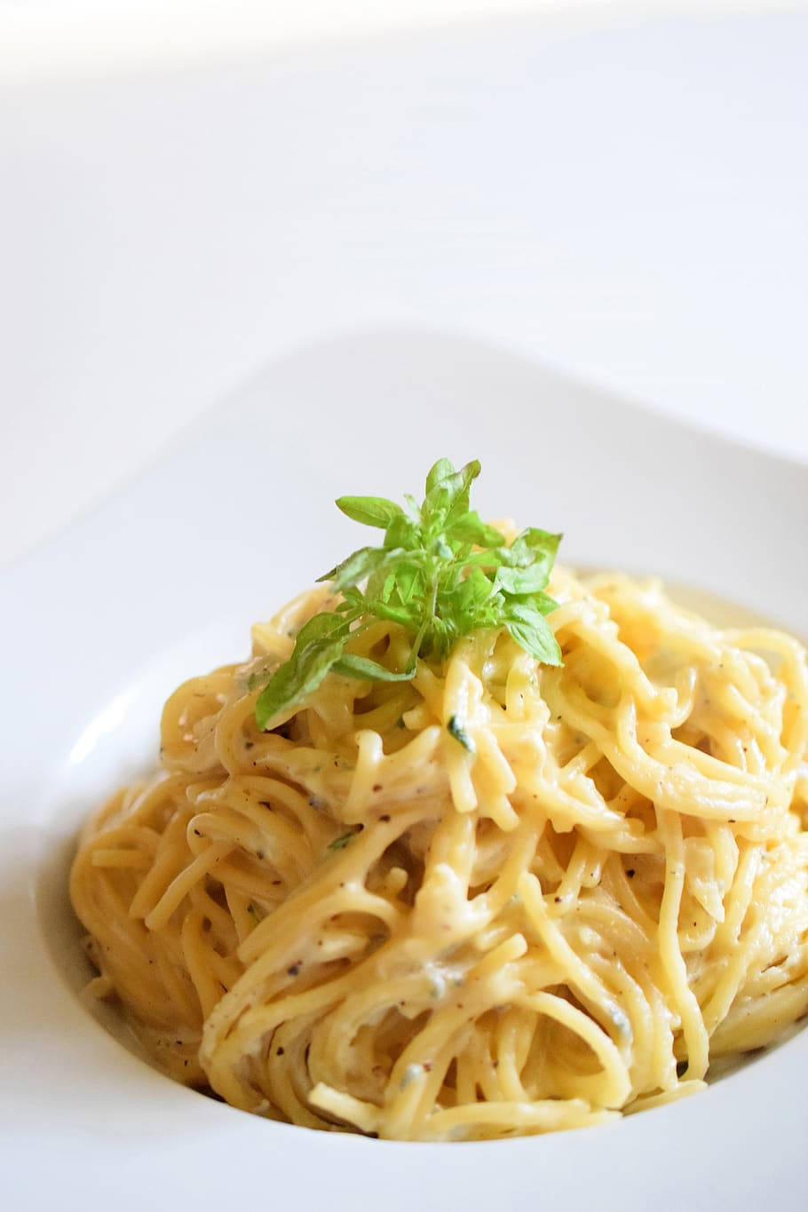 搭配歐芹的 Cacio E Pepe 壁紙 — 一盤奶油意粉配上新鮮羅勒，優雅地放在白色碗中，在柔和明亮的光線下。