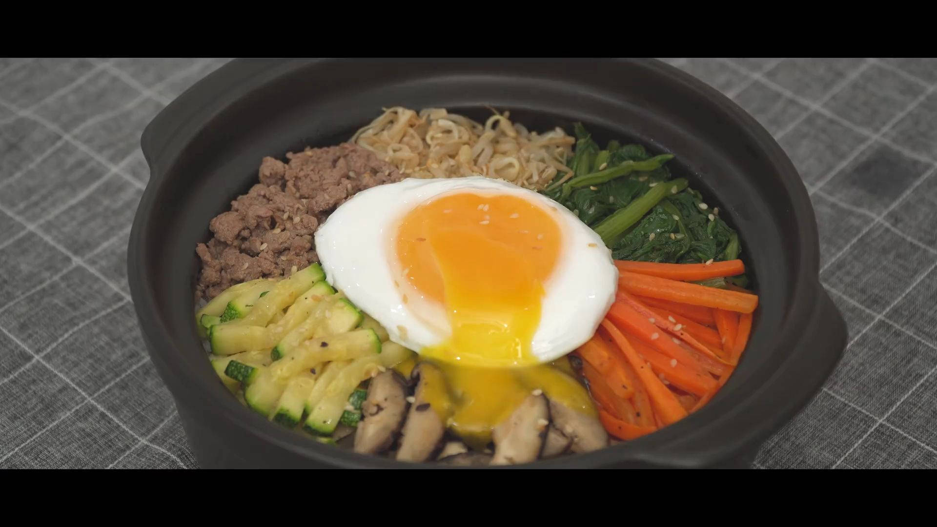 搭配流心蛋的美味拌飯 壁紙 — 一個冒煙的石鍋拌飯，上面放著一個完美流心的太陽蛋。