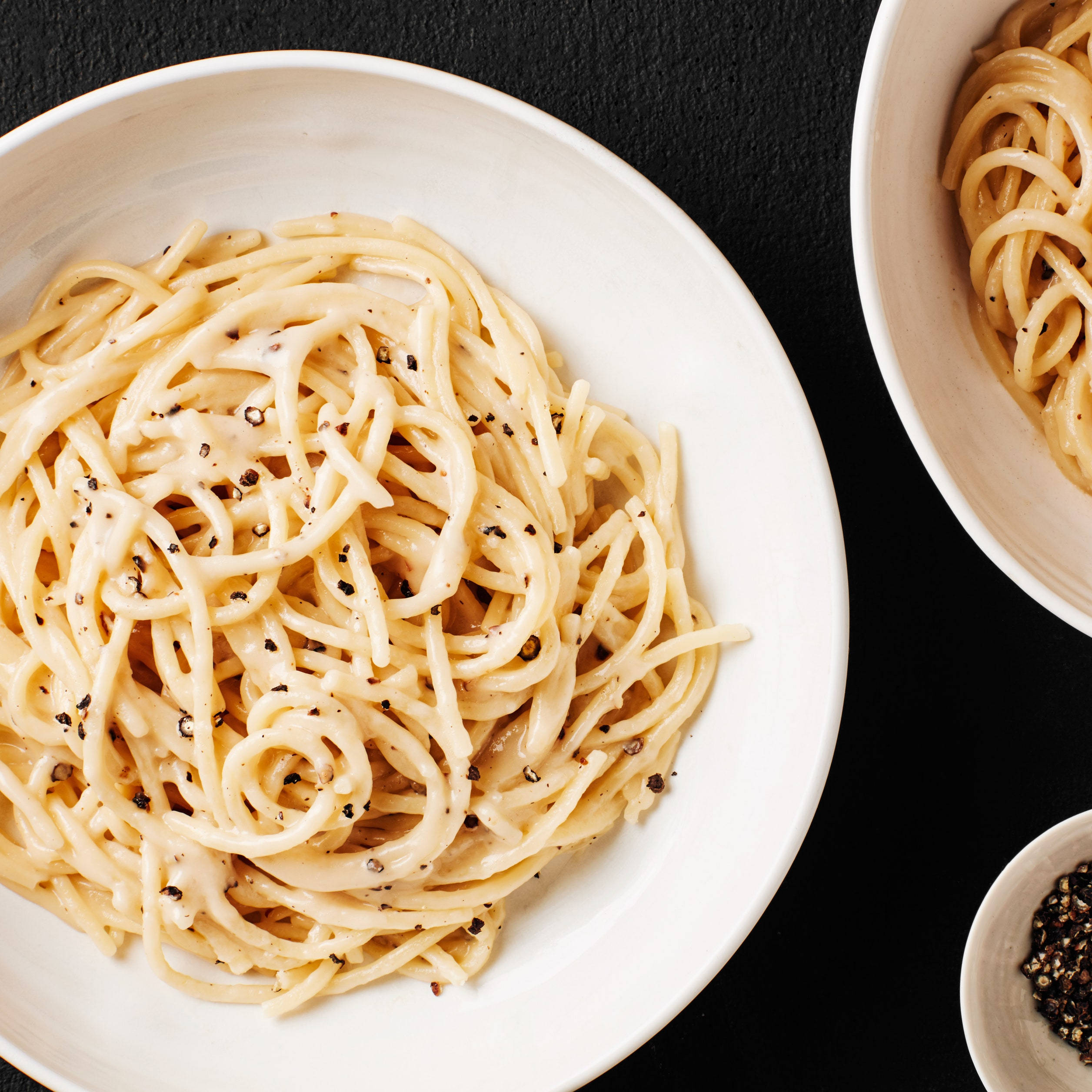搭配研磨黑胡椒的美味 Cacio E Pepe 壁紙 — 忌廉意粉配黑胡椒，盛載於白色碗中，置於深色紋理背景上。