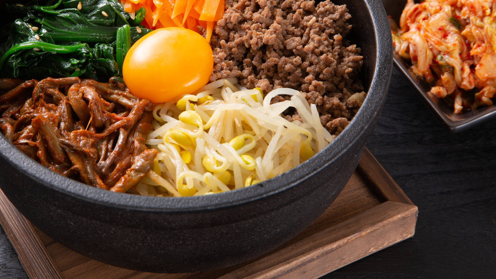 搭配碎牛肉的韓式拌飯 壁紙 — 一個冒煙的石鍋韓國拌飯，上面放有生雞蛋、豆芽、牛肉和菠菜，旁邊有泡菜。