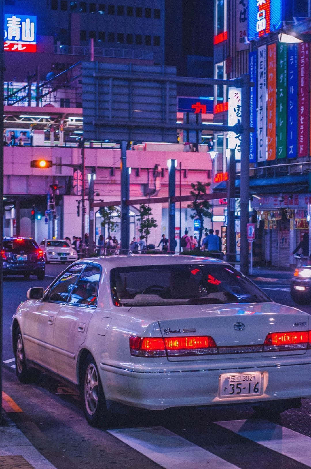 夜晚霓虹燈城市路口中的銀色汽車，閃爍招牌和濕滑路面。