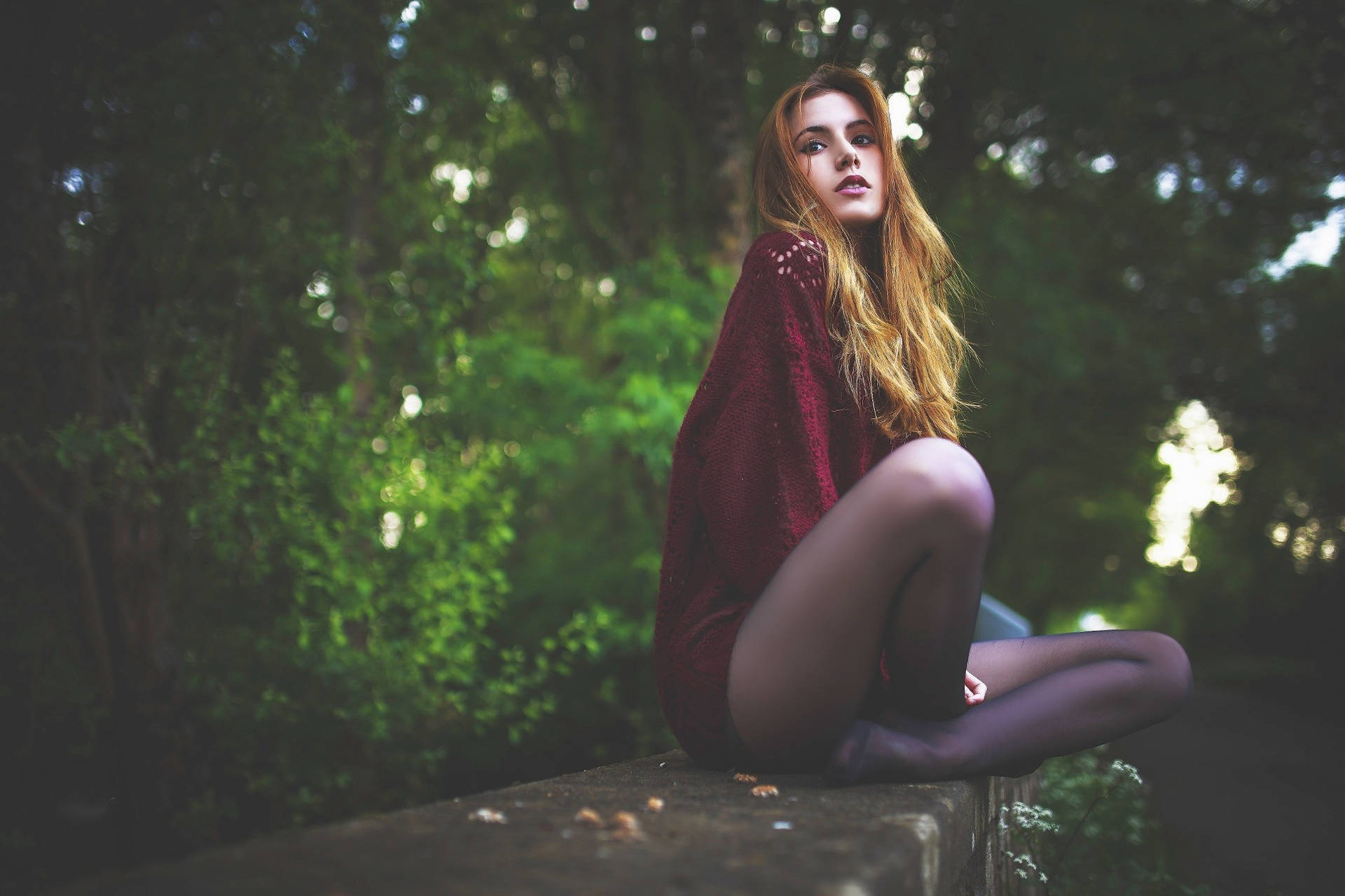 一位穿著紅色毛衣的女性坐在綠色森林中的石階上。