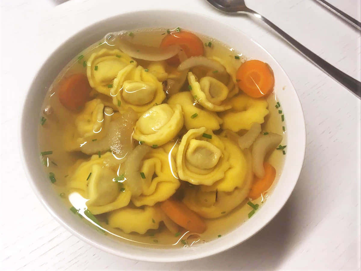 搭配胡蘿蔔的家常義式餃子湯 壁紙 — 一碗熱騰騰的意大利餃子湯，配有紅蘿蔔、洋蔥和新鮮香草，清湯底。
