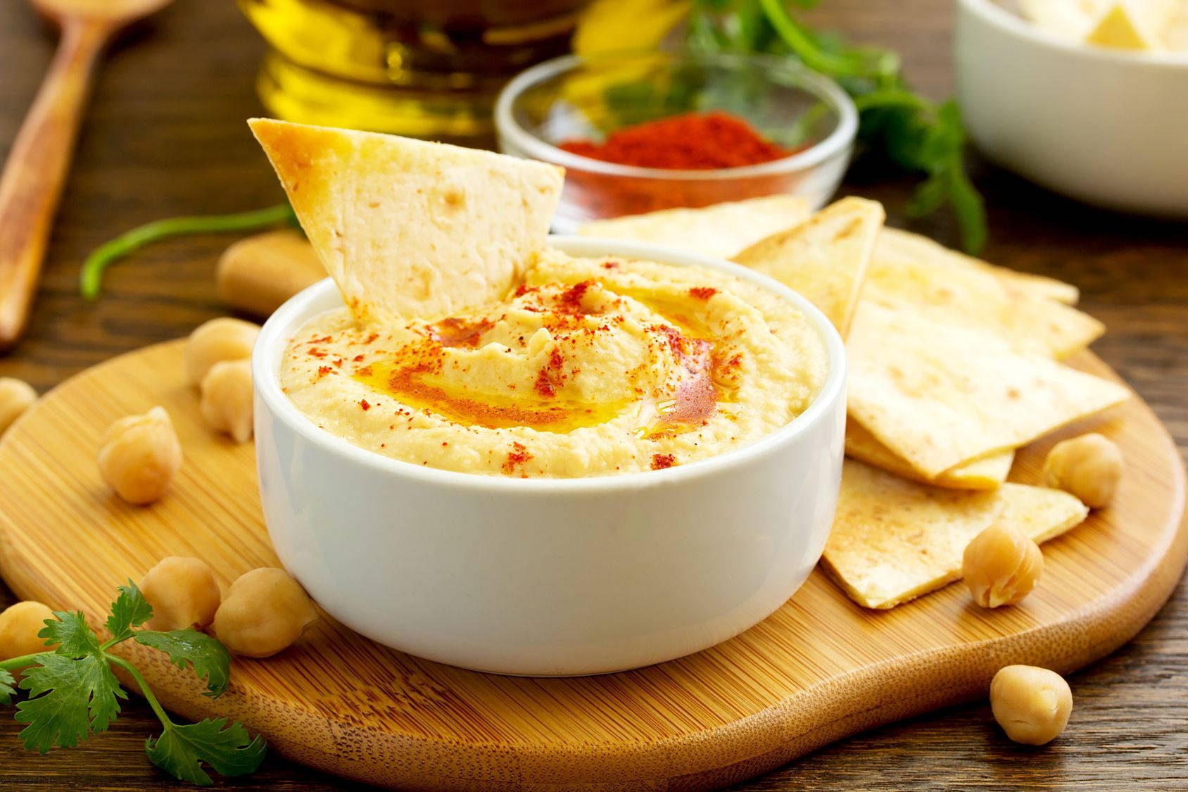 搭配酥脆薯片的美味鵝肝醬蘸醬 壁紙 — 白色碗中的奶油鷹嘴豆泥，飾以紅椒粉和橄欖油，配上皮塔餅乾和鷹嘴豆，放在木板上。