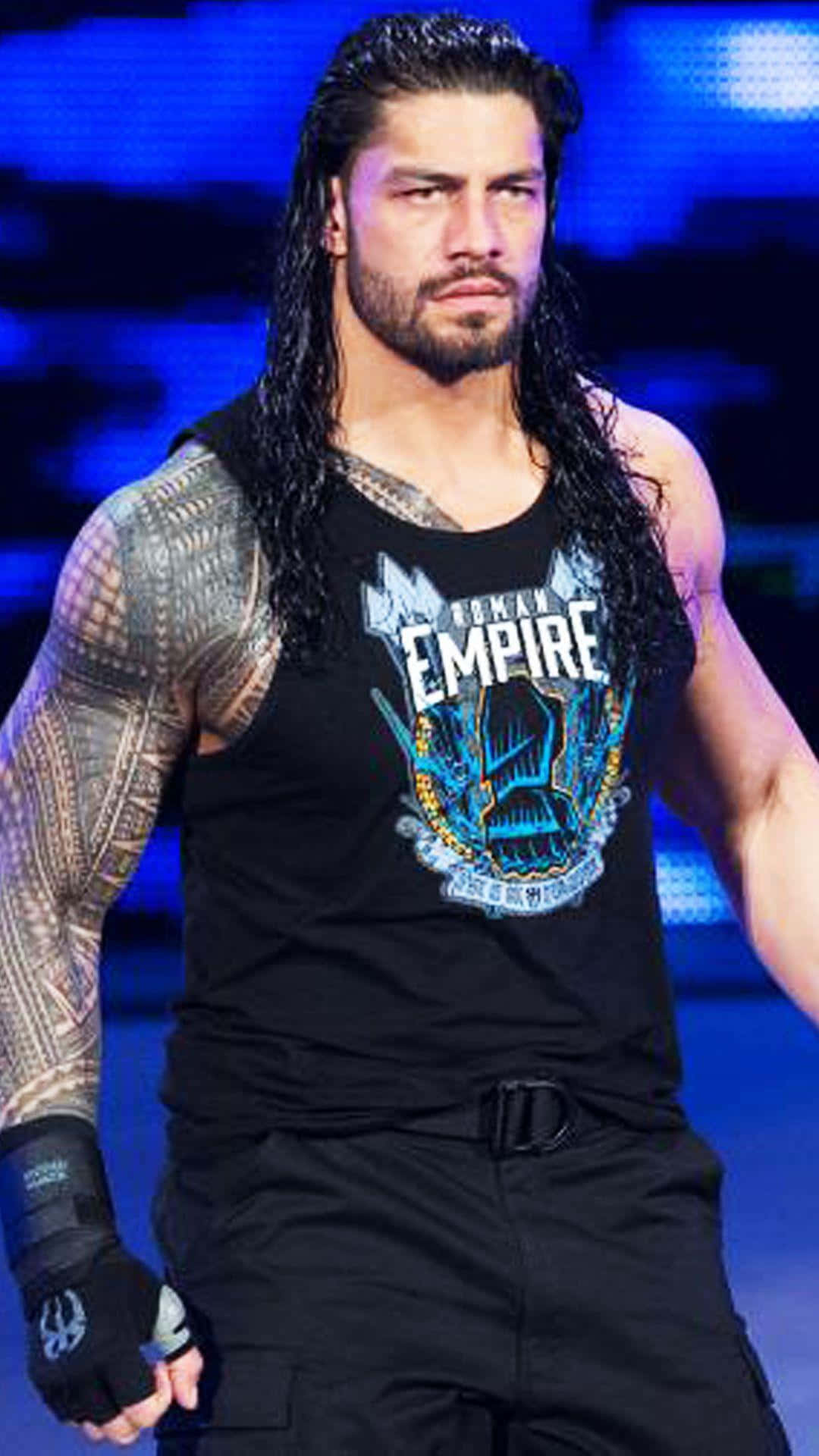 Roman Reigns 桌布 壁紙 — 摔角手 Roman Reigns 留著長黑髮和紋身，在藍色舞台燈光下穿著黑色背心，眼神銳利。
