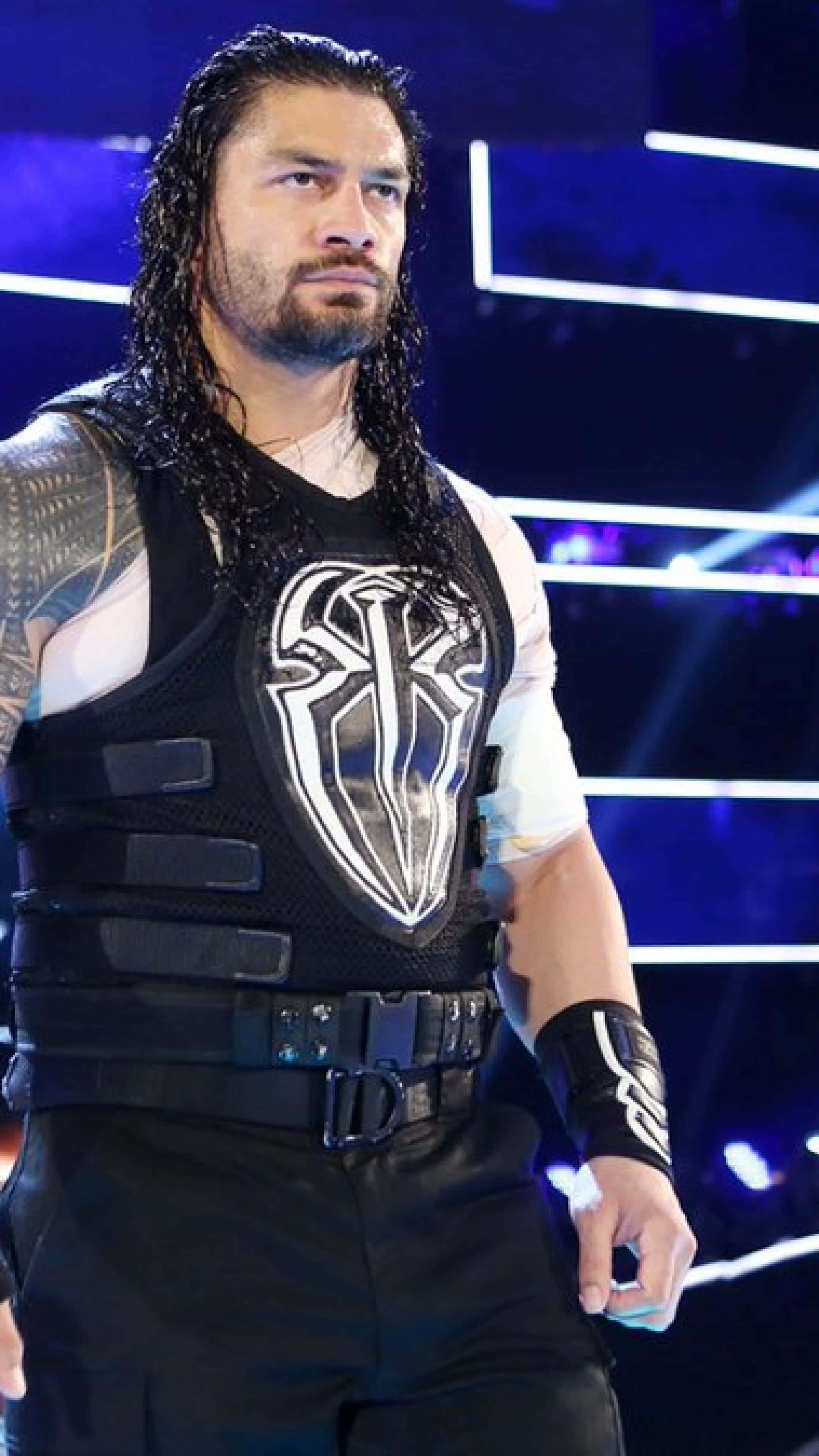 Roman Reigns 桌布 壁紙 — 摔角手 Roman Reigns 自信地站在明亮的舞台燈光下，身穿帶有白色部落標誌的黑色背心。