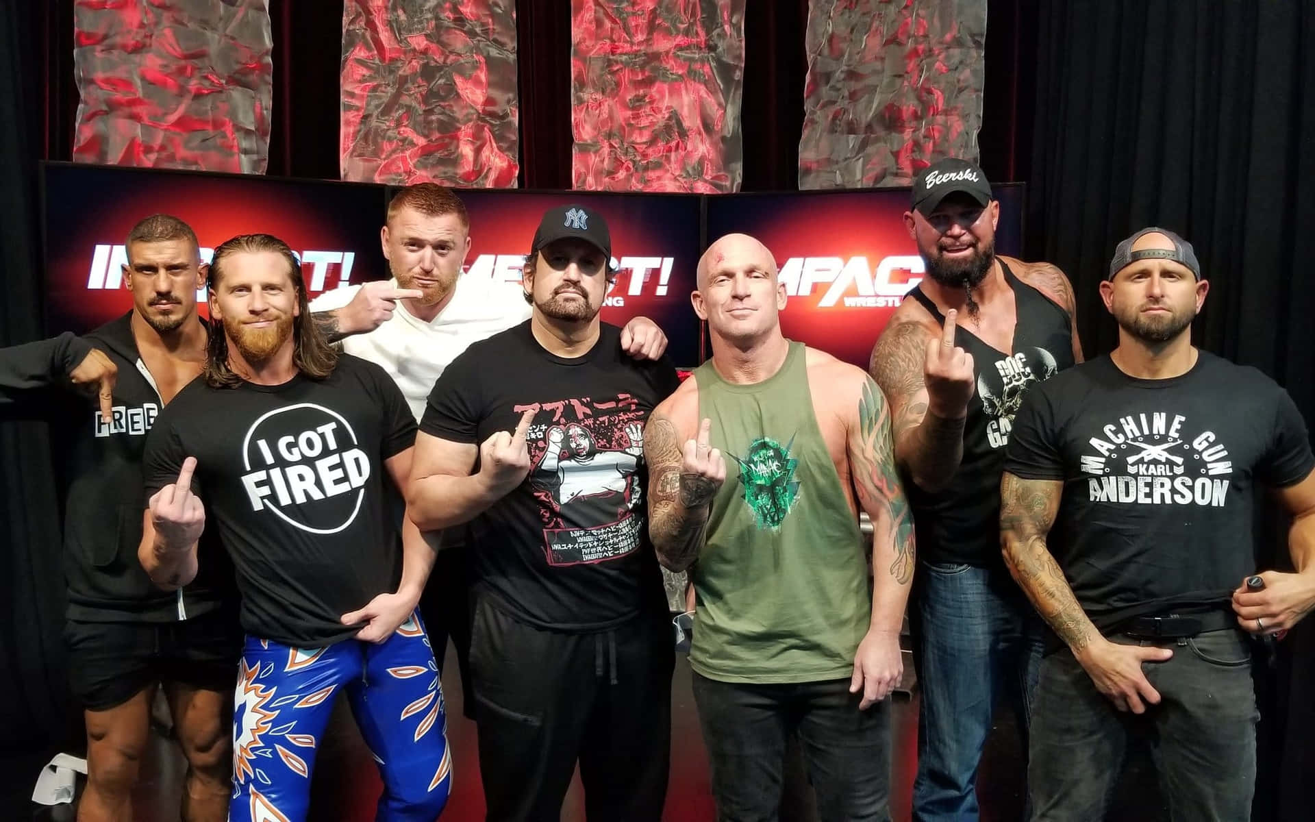 七位摔角手在 IMPACT Wrestling 背景前以挑釁姿態擺姿勢。