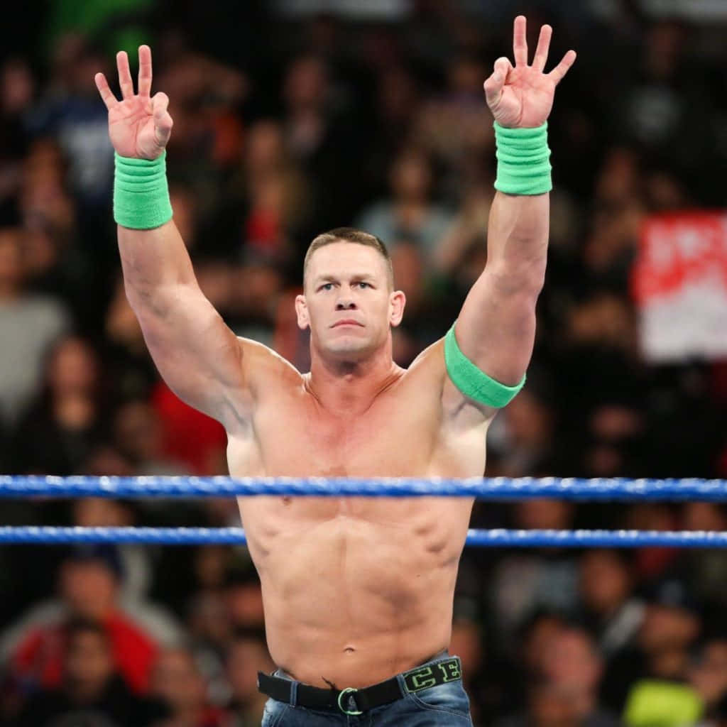 John Cena 桌布 壁紙 — 摔角手約翰·辛納在擂台上高舉雙臂，戴著綠色腕帶和牛仔褲，展現勝利姿態。