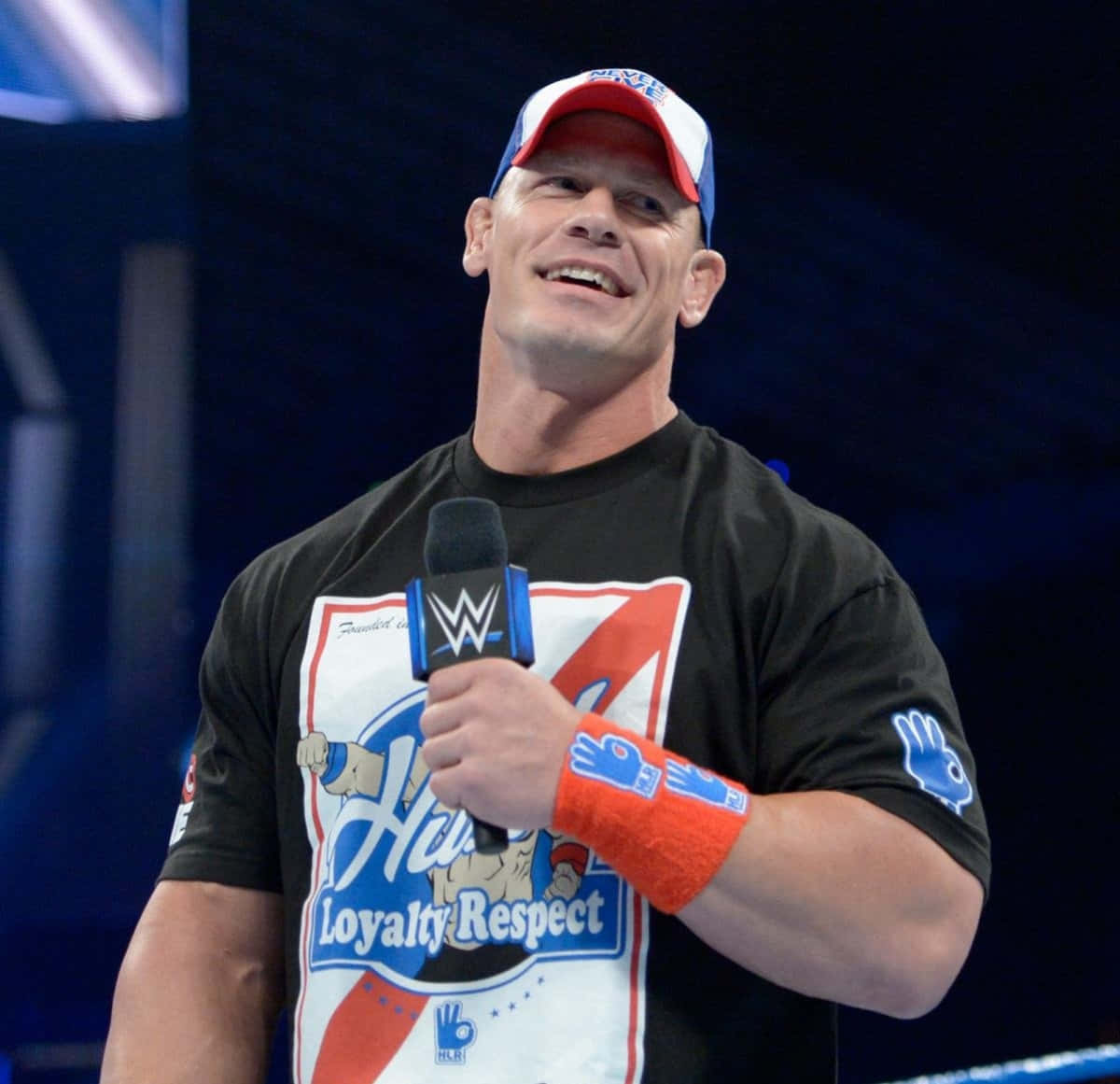 John Cena 桌布 壁紙 — 摔角手約翰·辛納在明亮的場館燈光下，在擂台上自信地微笑，手持WWE麥克風。