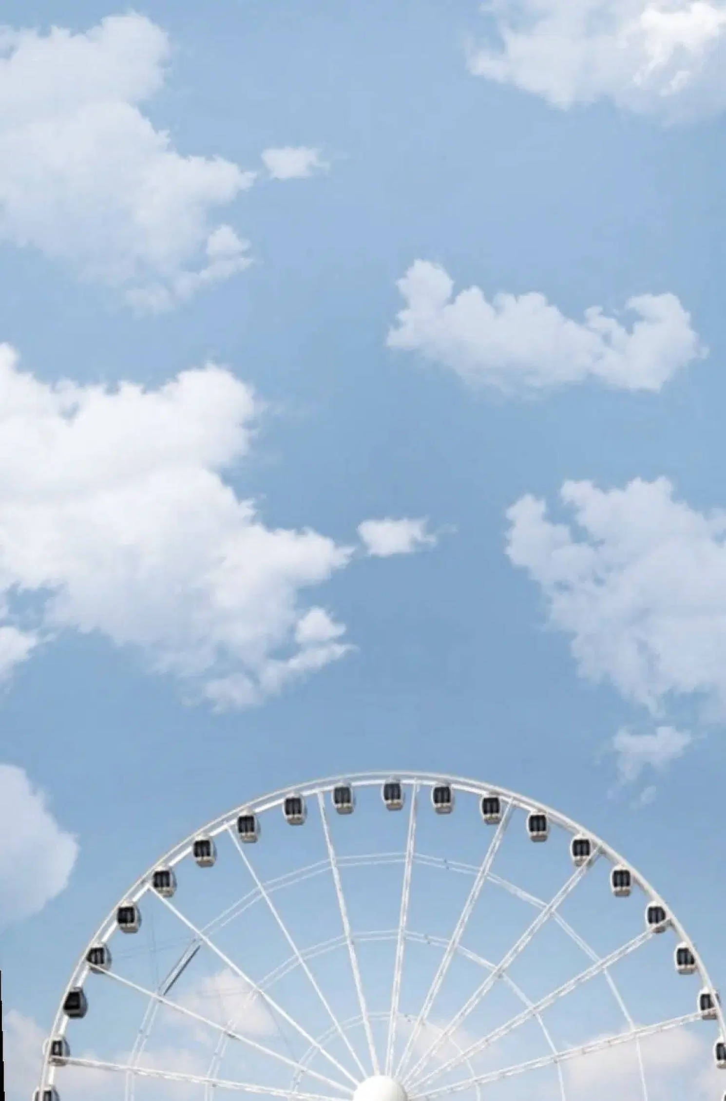 摩天摩天輪與粉藍天空背景 壁紙 — 一個白色摩天輪在點綴著蓬鬆白雲的明亮藍天下劃出弧線。