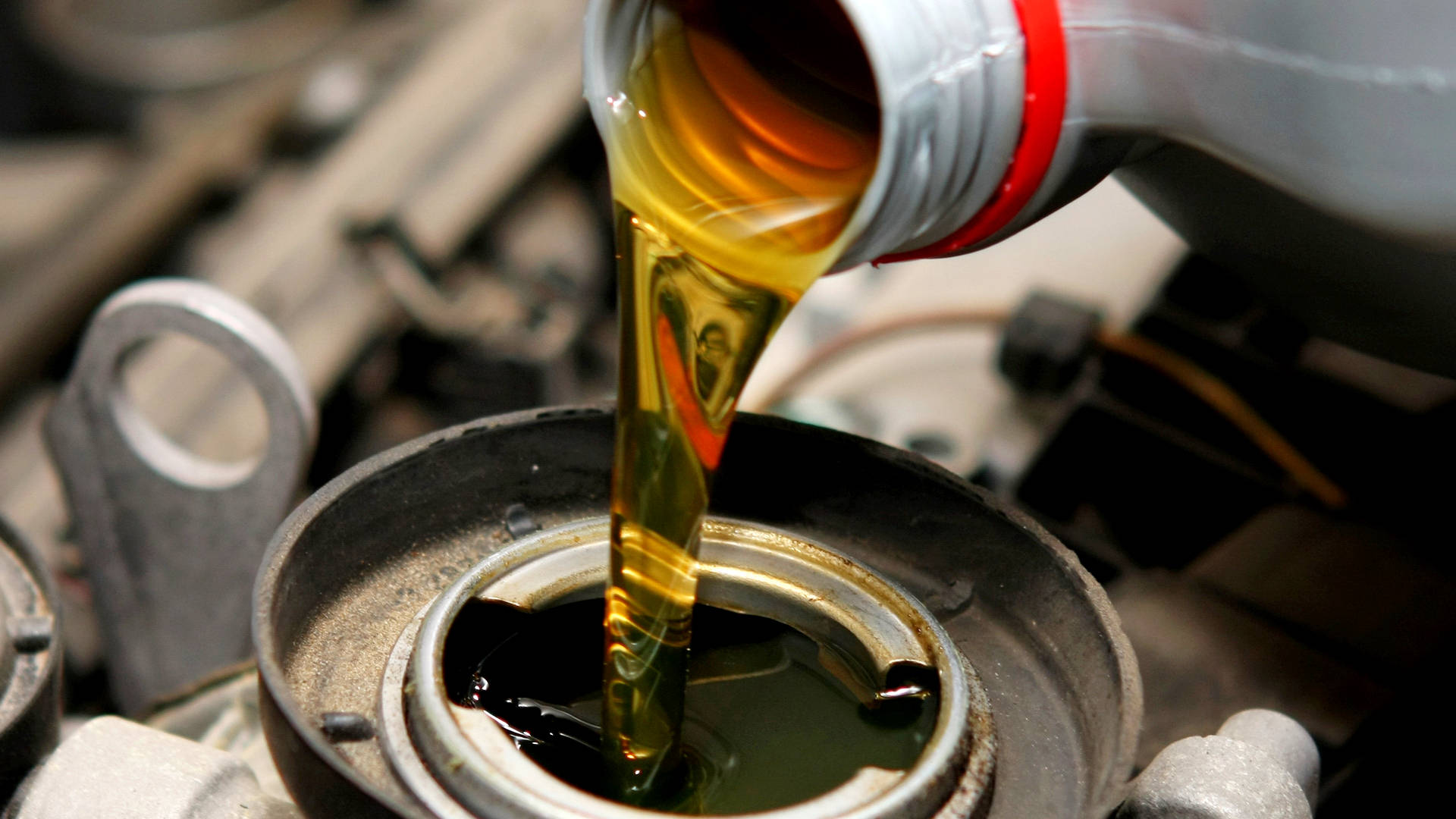 摩托引擎油 壁紙 — 金色引擎機油從瓶子平穩地倒入開放的引擎曲軸箱中，周圍是機械部件。