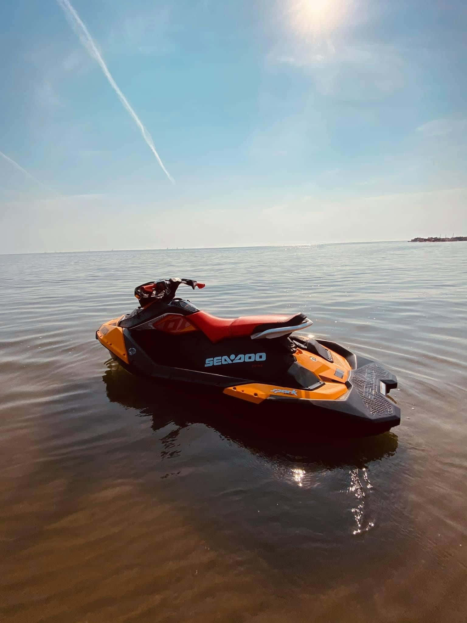 摩托艇與陽光 壁紙 — 一架黑色和橙色的 Sea-Doo 水上電單車在平靜的棕色水面上漂浮，天空湛藍，有凝結尾跡。