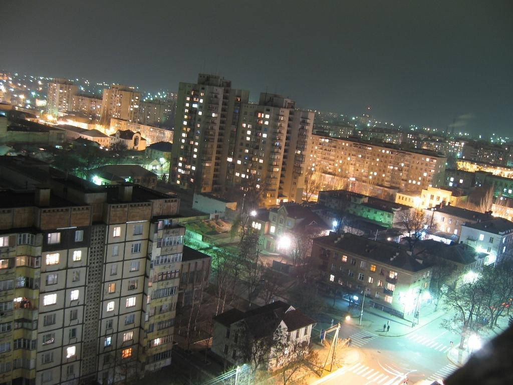 摩爾多瓦城市夜景 壁紙 — 高角度夜間景觀，密集的城市社區，有燈光照射的公寓大樓和路燈在寧靜的街道上投射溫暖的光芒。