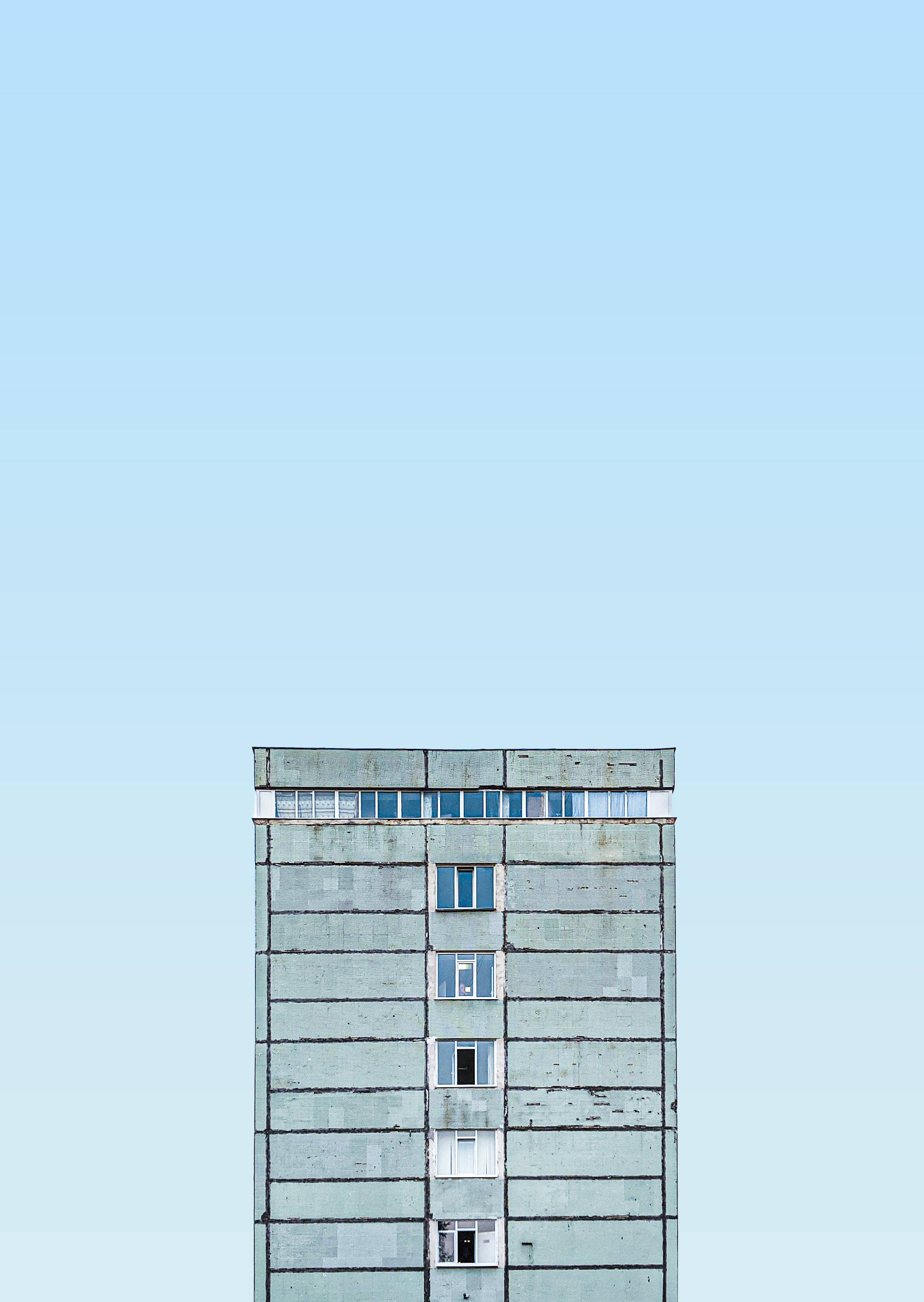 摩爾多瓦基希納烏灰色建築 壁紙 — 一座風化的混凝土公寓大樓，在廣闊的淡藍色天空下，以極簡的建築線條高高聳立。