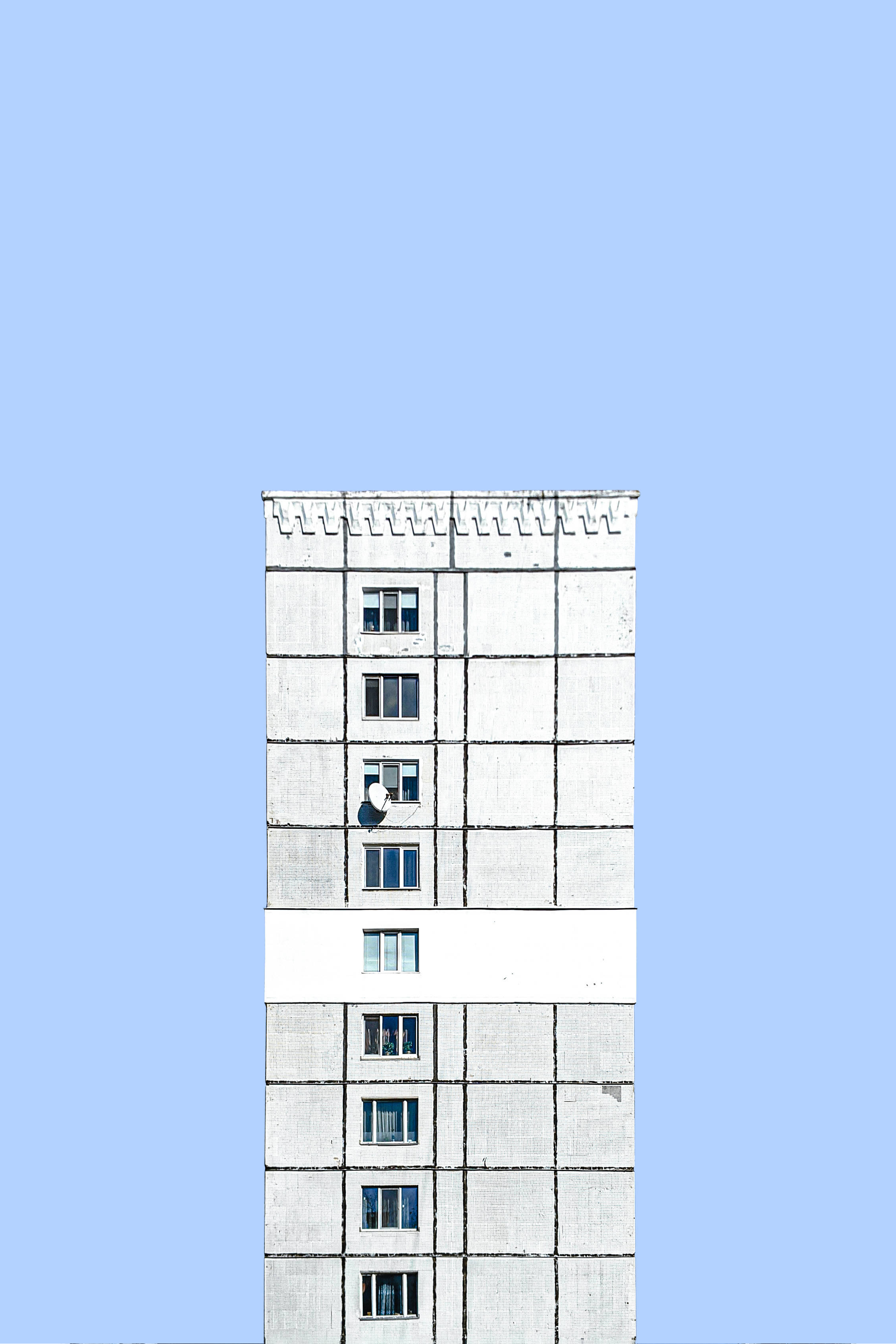 摩爾多瓦基希納烏灰色建築 壁紙 — 一座純白色的高層建築聳立在清澈的淡藍色天空中，窗戶裡可以看到一個人。